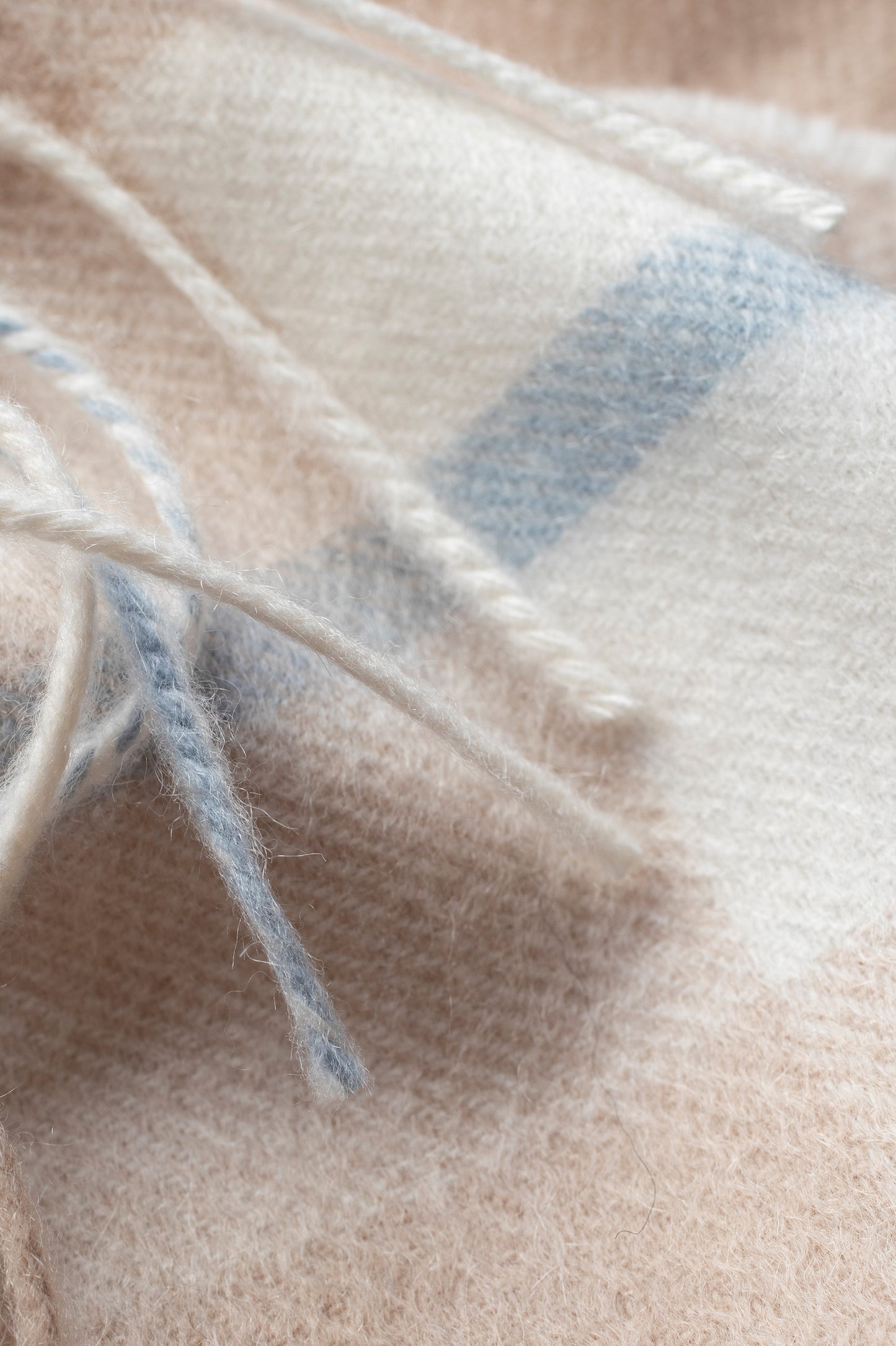 Close-up of Contemporary Check Cashmere Scarf in Champagne Pink showing soft wool texture, fringe detail, and blue check pattern