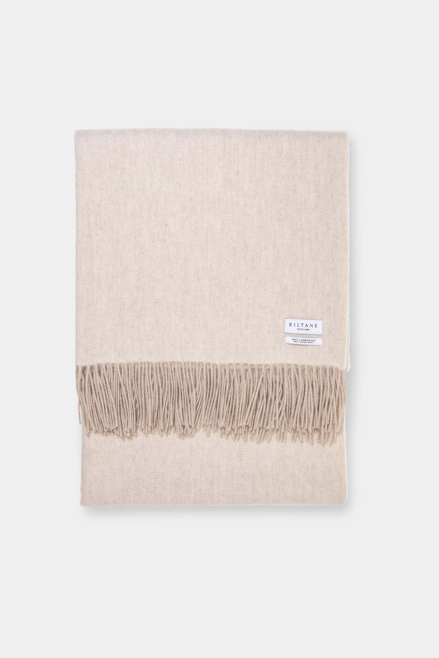 Kiltane Herringbone Lambswool Throw in Sand, folded flat showing soft beige herringbone weave and fringed edges