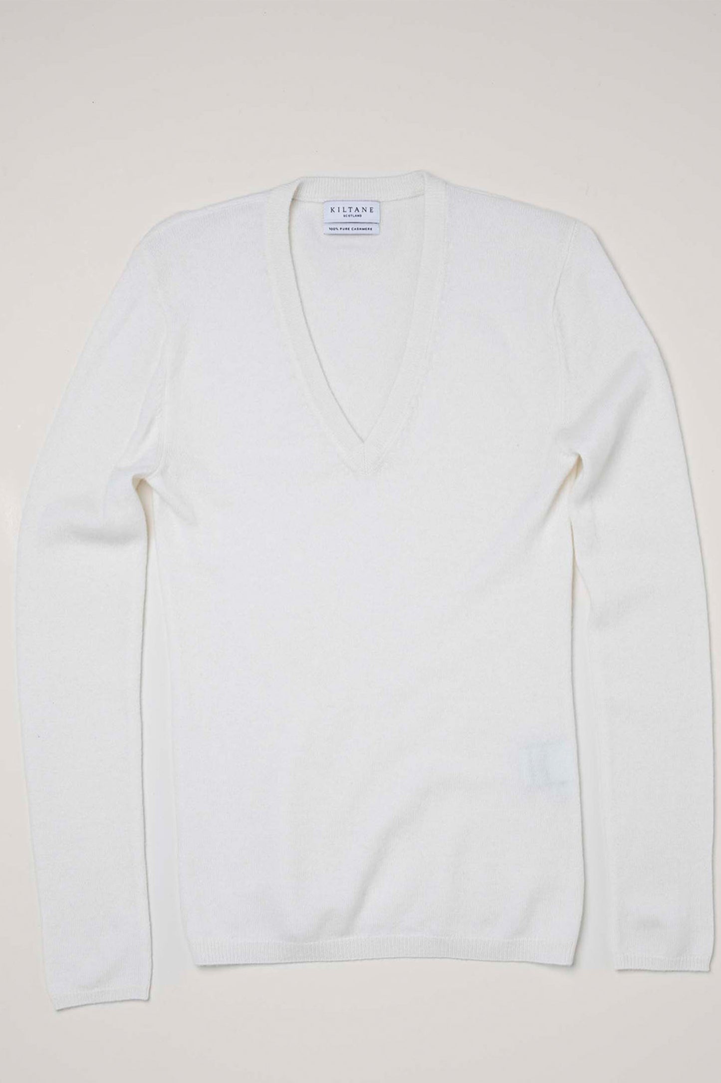 Kiltane Women's Cashmere V Neck Jumper in Soft Cream laid flat, showing the deep V neckline and brand label detail