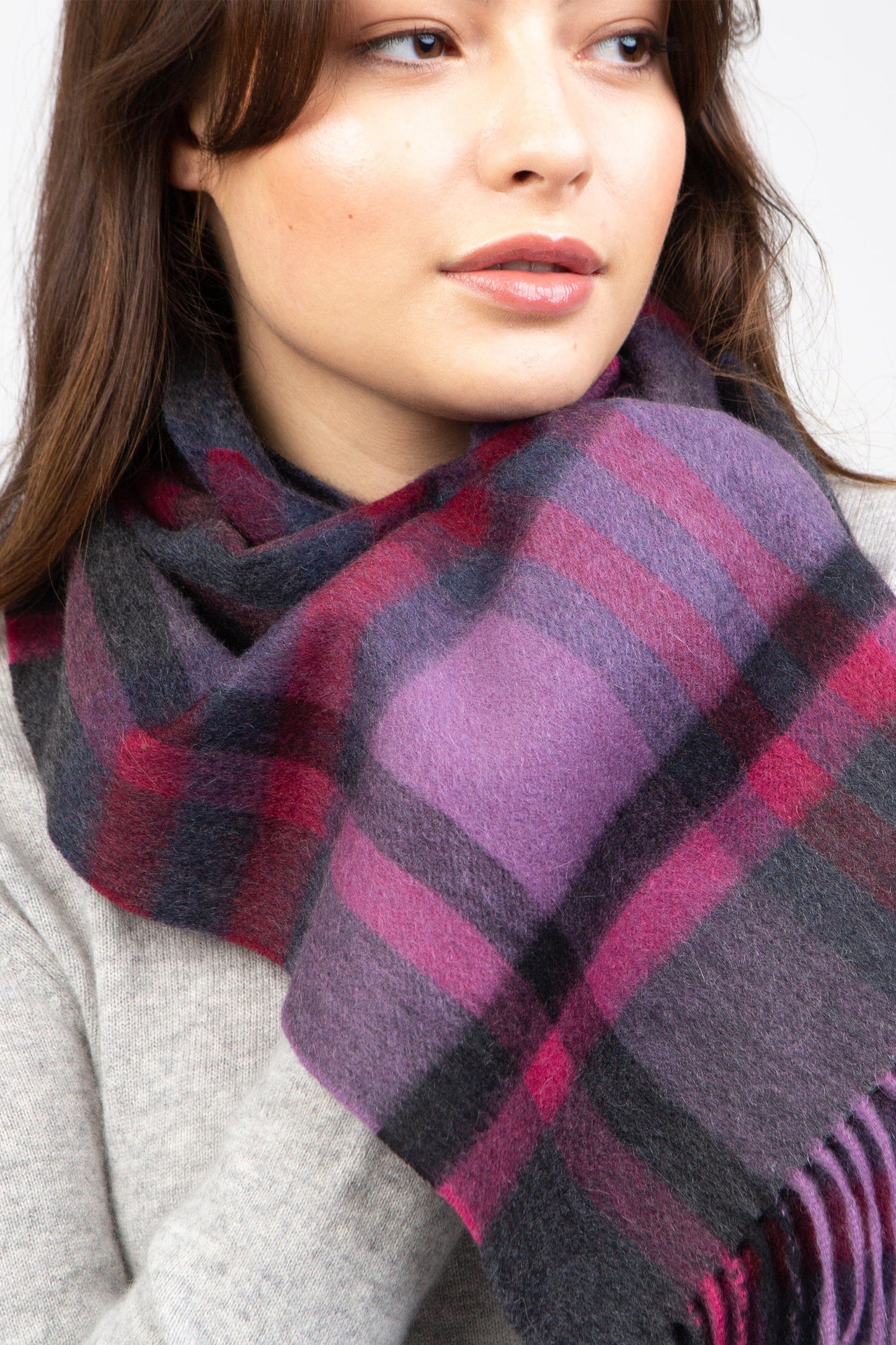 Tartan 2 Lambswool Scarf in Deep Purple worn loosely around the neck, showing plaid pattern in purple, charcoal, and red with fringed ends
