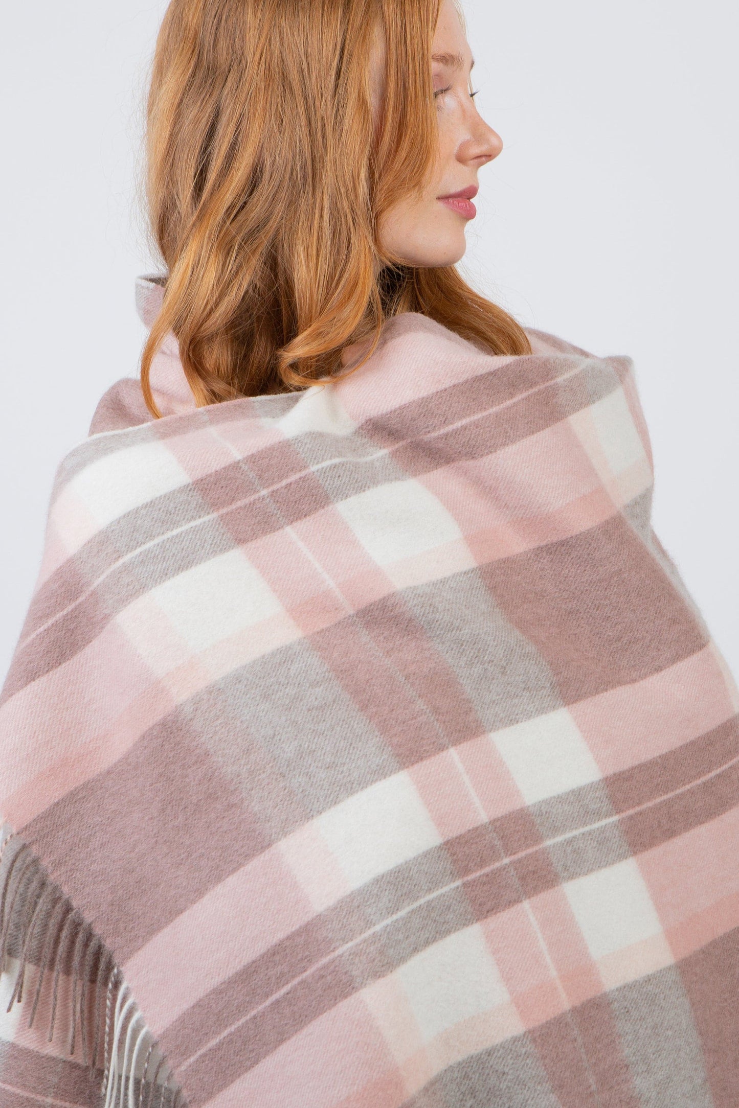 Contemporary Check Lambswool Stole in Cameo draped over shoulders, showing pink, grey, and cream plaid pattern with fringed edge