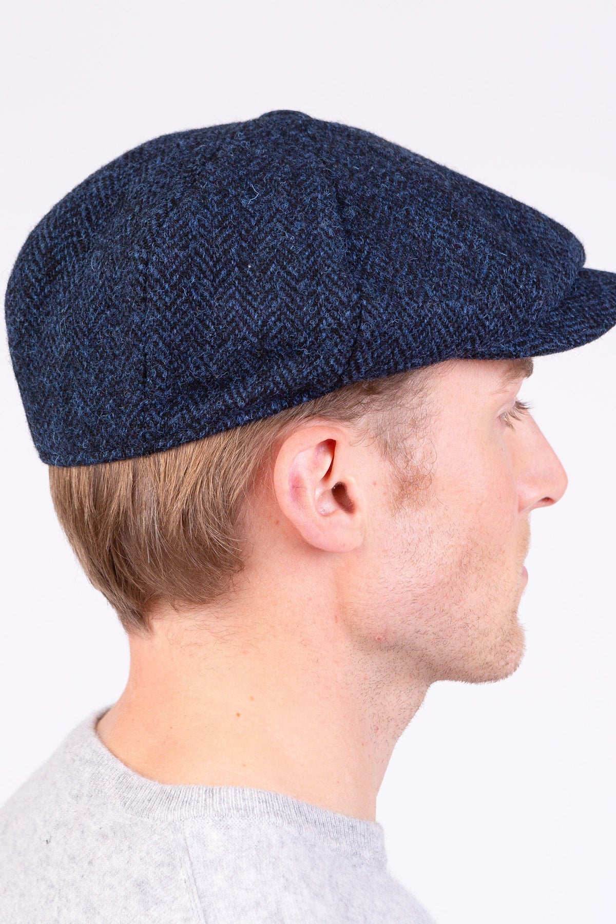 Harris Tweed Carloway Hat in Dark Navy Herringbone — side profile view worn by model showing flat cap shape and tweed texture