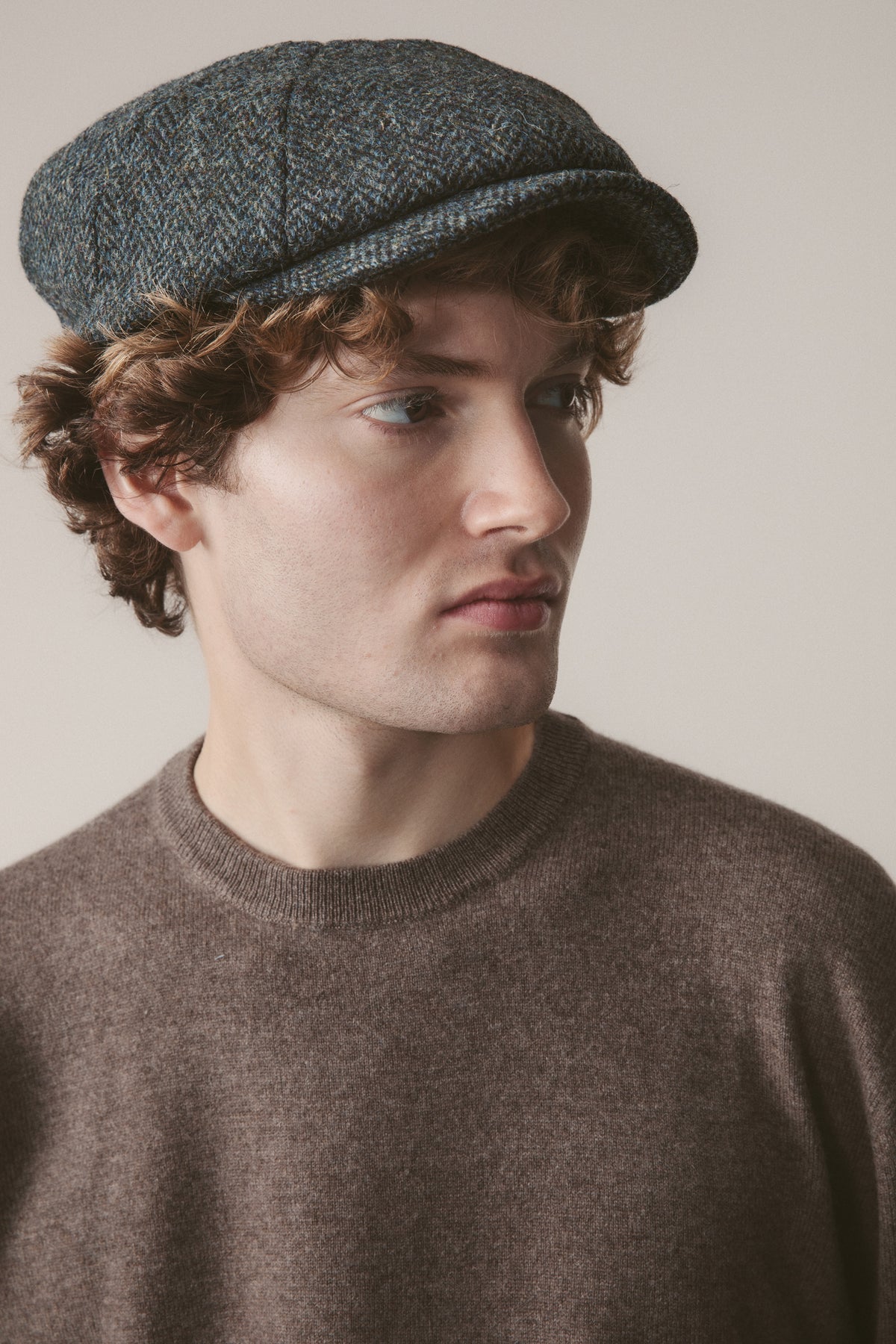 Harris Tweed Carloway Hat in Blue Mix Herringbone worn by model, three-quarter front view showing flat cap shape and tweed texture