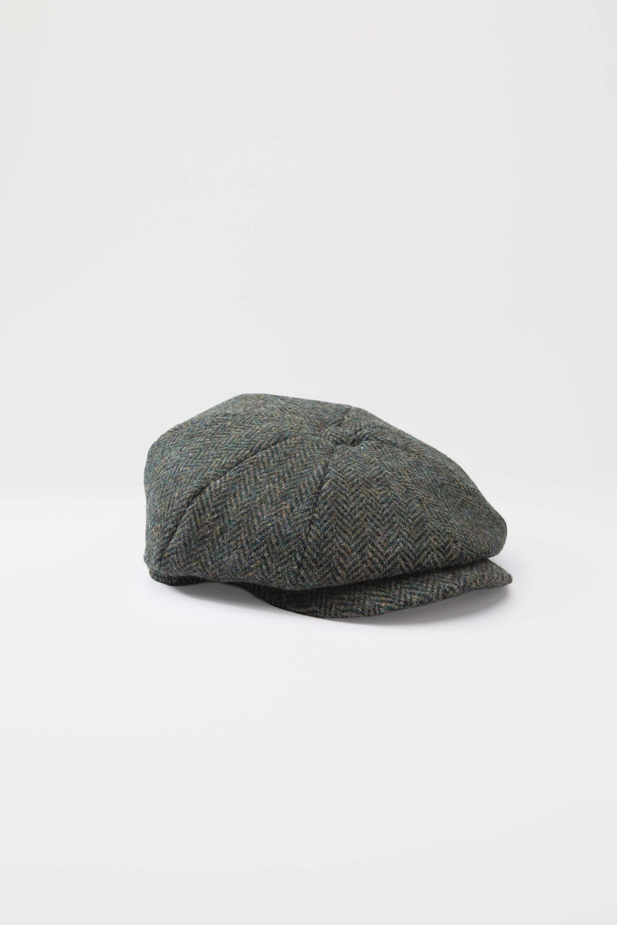 Harris Tweed Carloway Hat in dark green herringbone, three-quarter front view showing eight-panel newsboy crown and short brim
