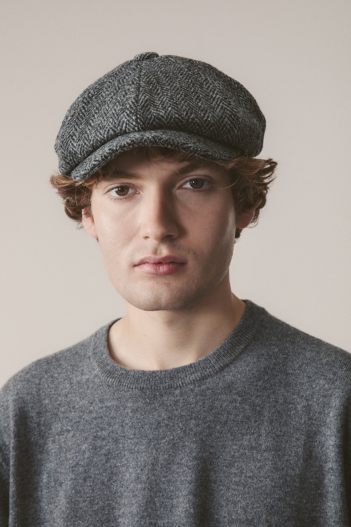 Harris Tweed Carloway Hat in charcoal herringbone, bakerboy-style cap with panelled crown and short brim, worn by model