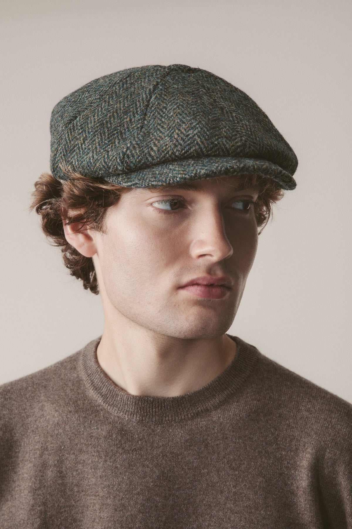 Harris Tweed Carloway Hat in dark green herringbone wool, bakerboy flat cap style, worn by model with brown sweater