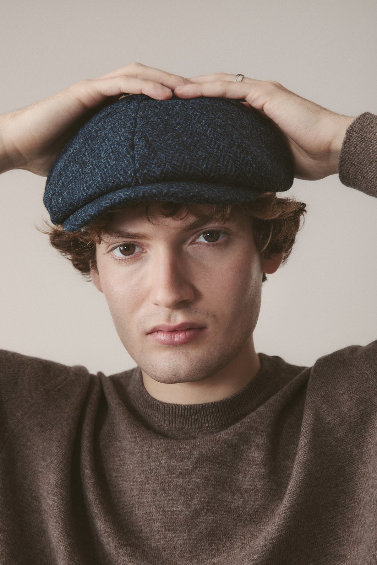 Harris Tweed Carloway Hat in dark navy blue herringbone, bakerboy-style flat cap modelled on a young man, front view