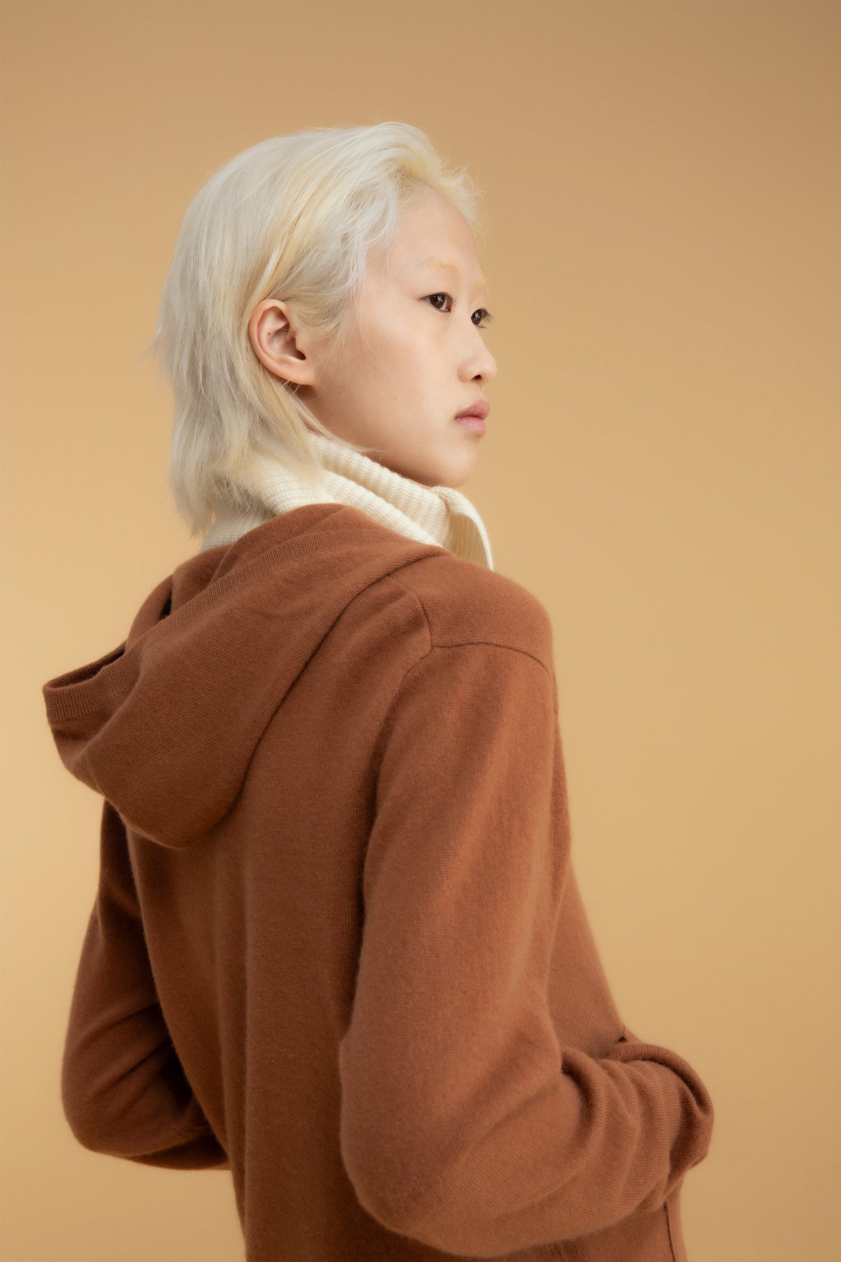 Knitted Cashmere Neck Tie in Cream worn as a turtleneck-style layer, visible above a brown hooded sweater