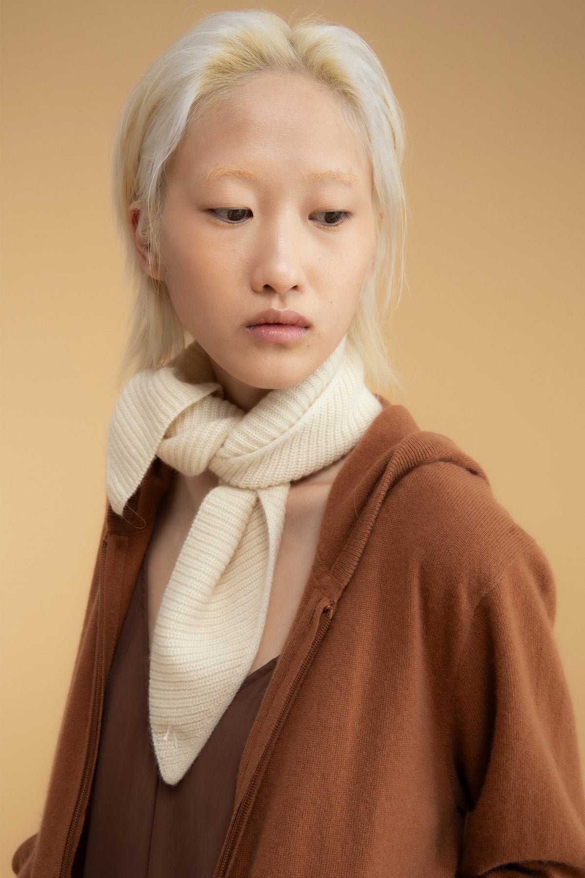 Knitted Cashmere Neck Tie in Cream styled knotted at the neck, worn with a brown zip-up hoodie