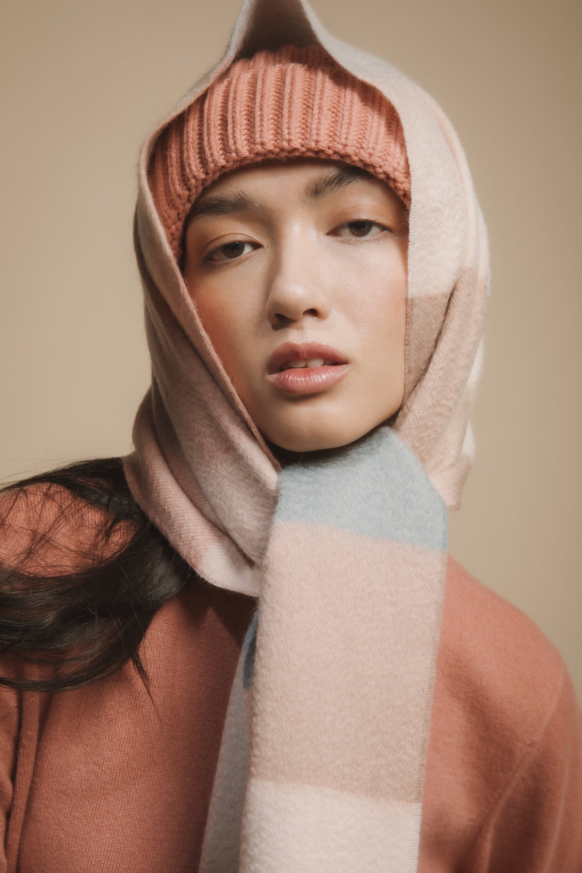 3 Square Check Cashmere Wide Scarf in Seashell worn wrapped over a ribbed beanie, showing pink, cream, and pale blue check pattern