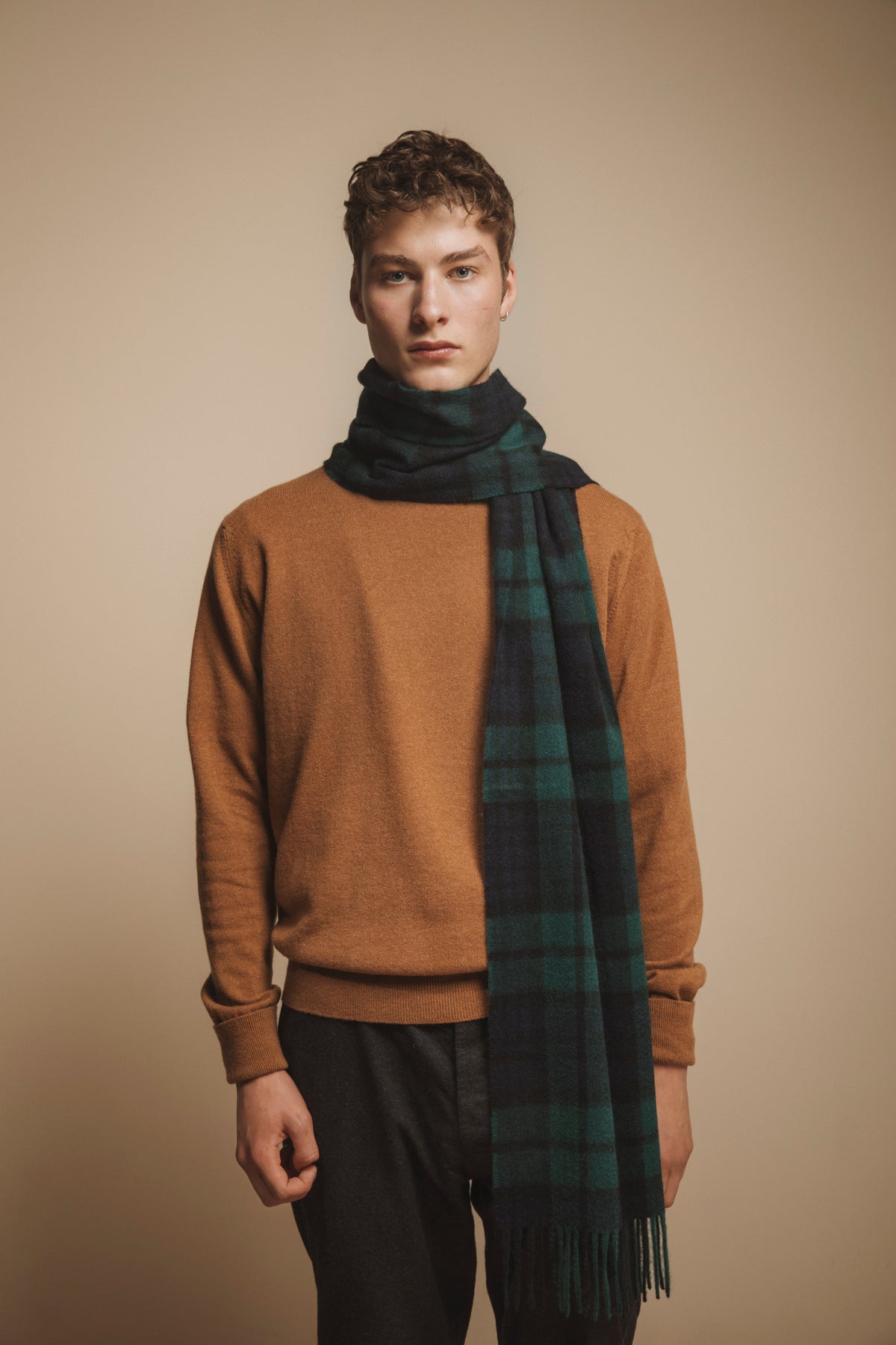 Made in Scotland Heritage Cashmere Wide Scarf in Blackwatch tartan worn looped around the neck over a camel sweater, showing fringe detail