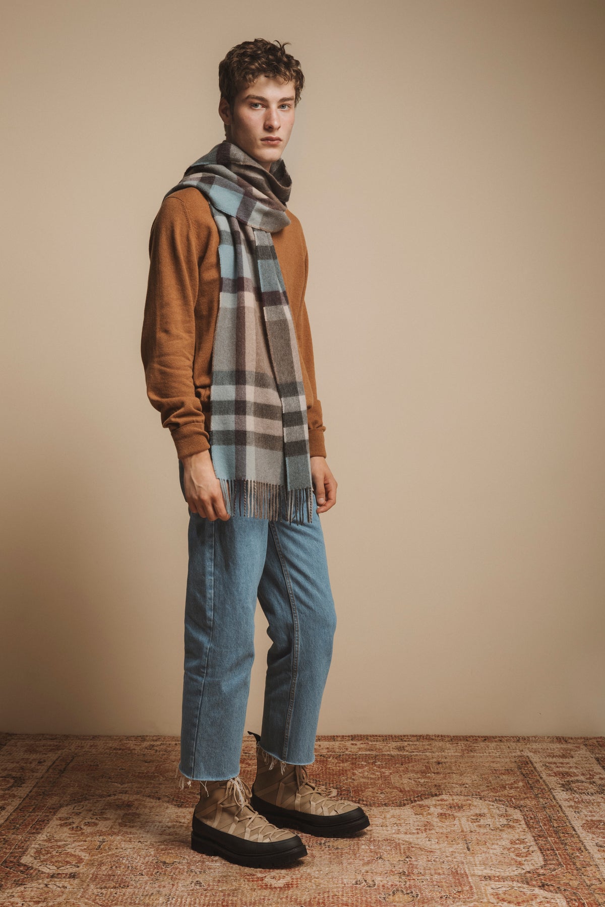 Made in Scotland Tartan 2 Cashmere Wide Scarf in Blue Taupe, worn draped over a camel sweater showing plaid pattern and fringe