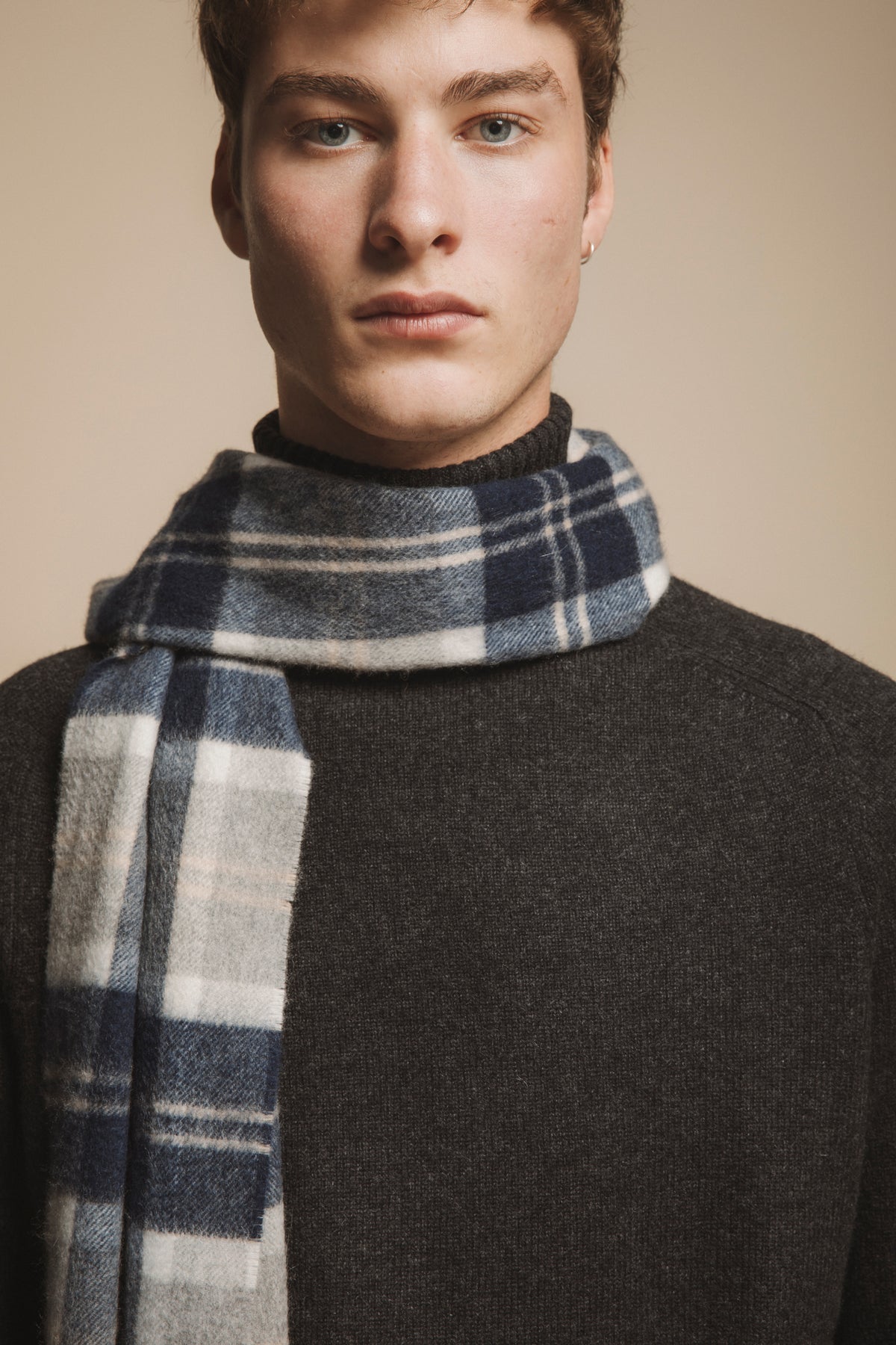 Model wearing the Heritage Cashmere Wide Scarf in Silver Bannockbane, showing navy and cream plaid pattern draped over a charcoal sweater