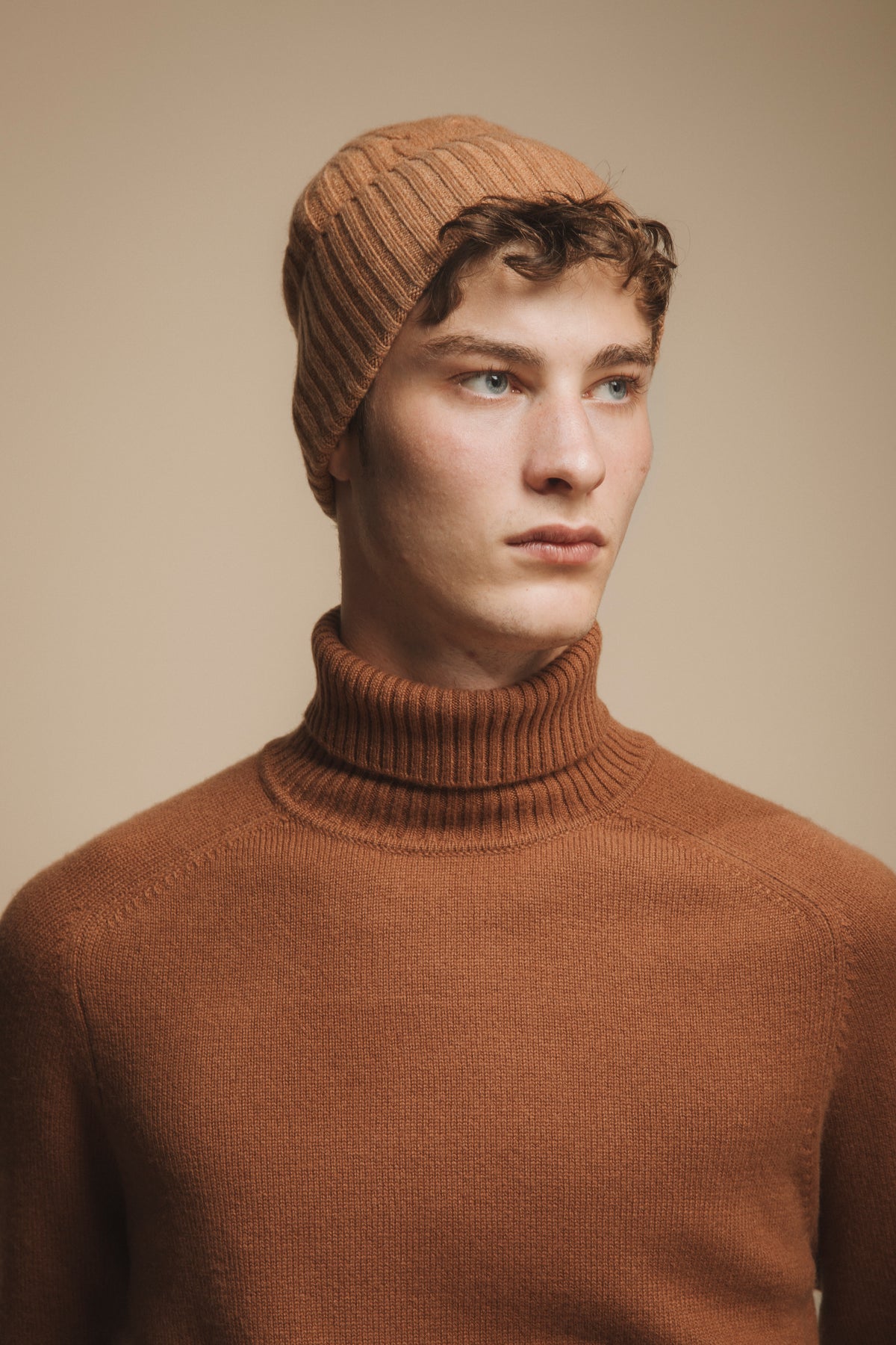 Cashmere Cable Beanie in Camel worn by model, featuring ribbed cable-knit texture and soft camel-tone finish