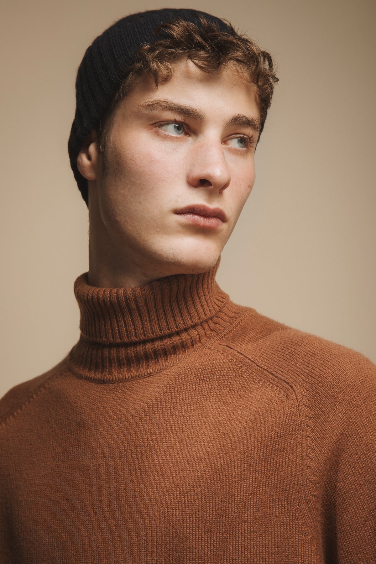 Cashmere Cable Beanie in Dark Navy worn pushed back on model's head, paired with a camel turtleneck sweater