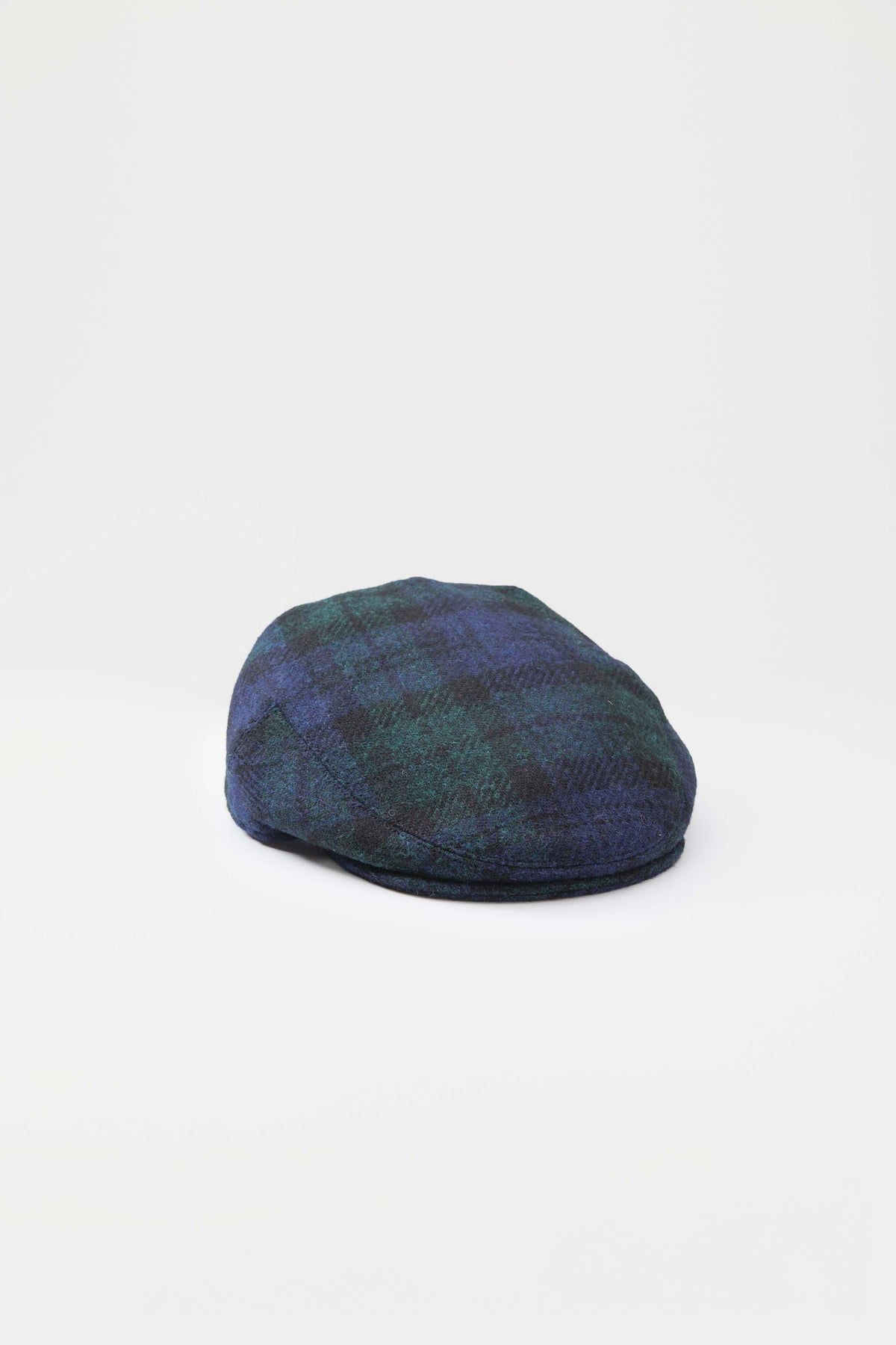 Harris Tweed Stornoway Cap in Blackwatch tartan — three-quarter front view showing green and navy plaid wool pattern