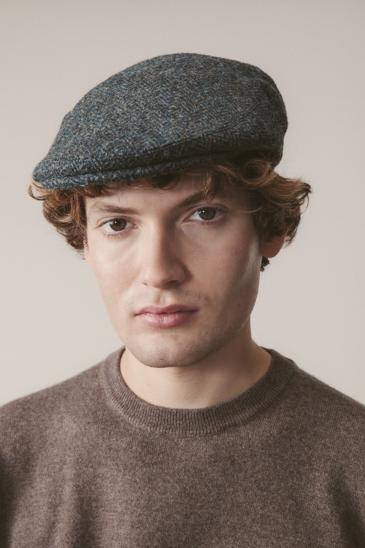 Harris Tweed Stornoway Cap in Blue Mix Herringbone worn by model, front view showing flat cap profile and tweed texture