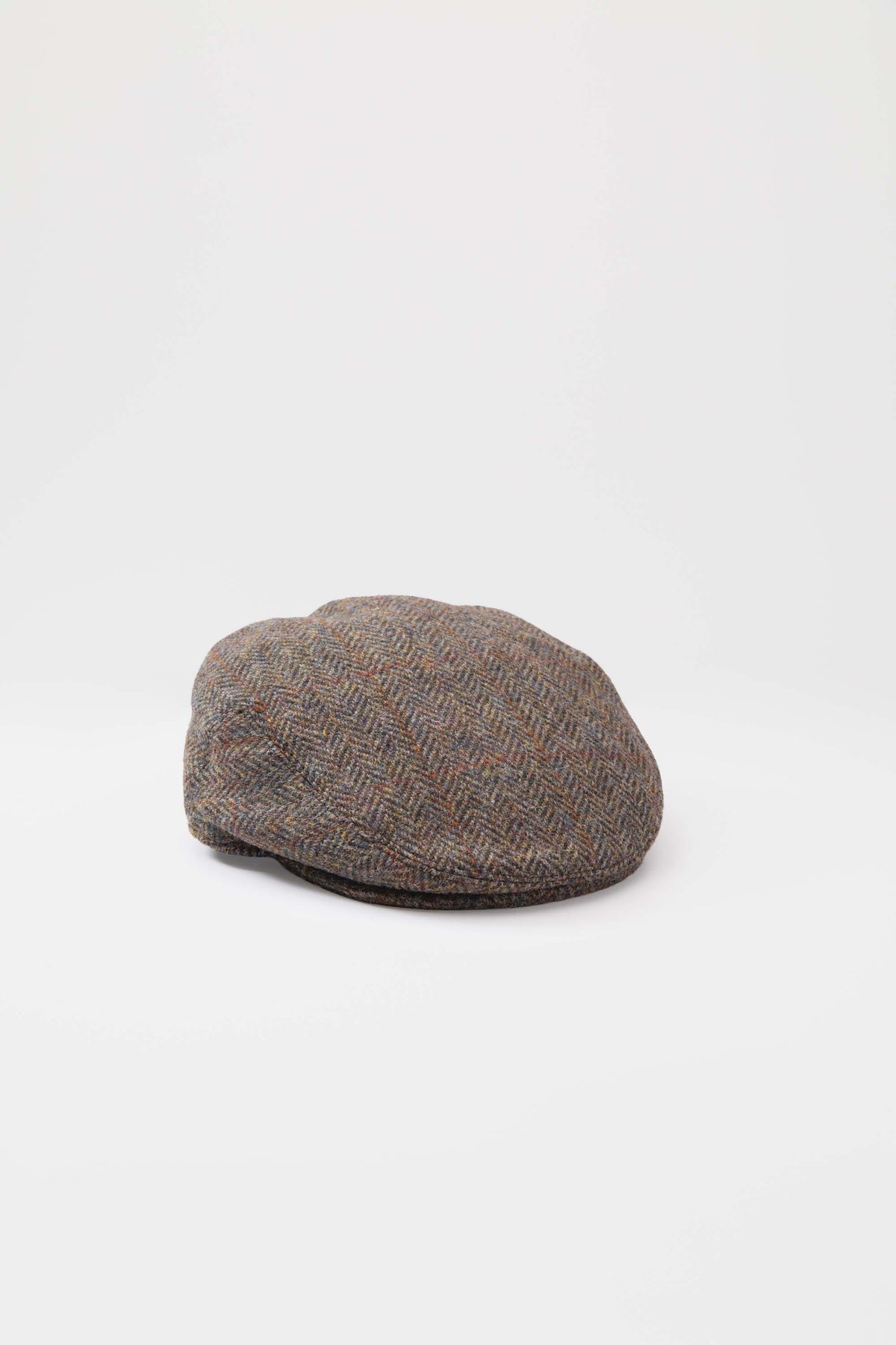 Harris Tweed Stornoway Cap in brown check herringbone wool, three-quarter top-down view showing crown shape and brim