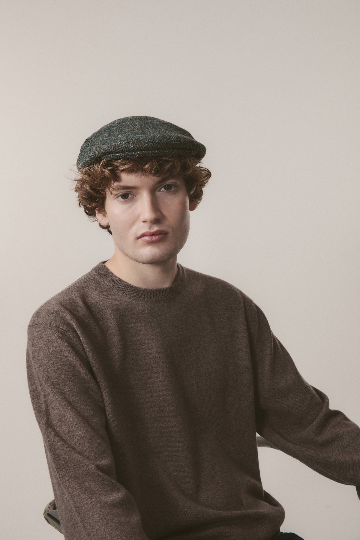 Harris Tweed Stornoway Cap in dark green herringbone flat cap style with stitched peak, worn by model in studio