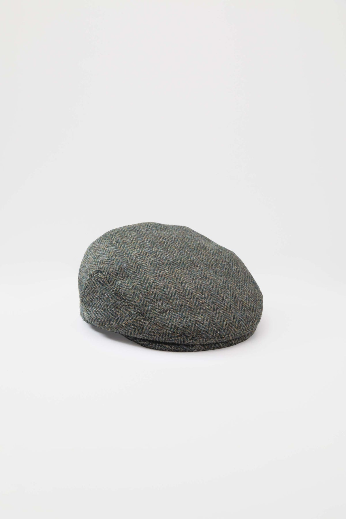 Harris Tweed Stornoway Cap in dark green herringbone, top-down angled view showing the flat crown and woven texture