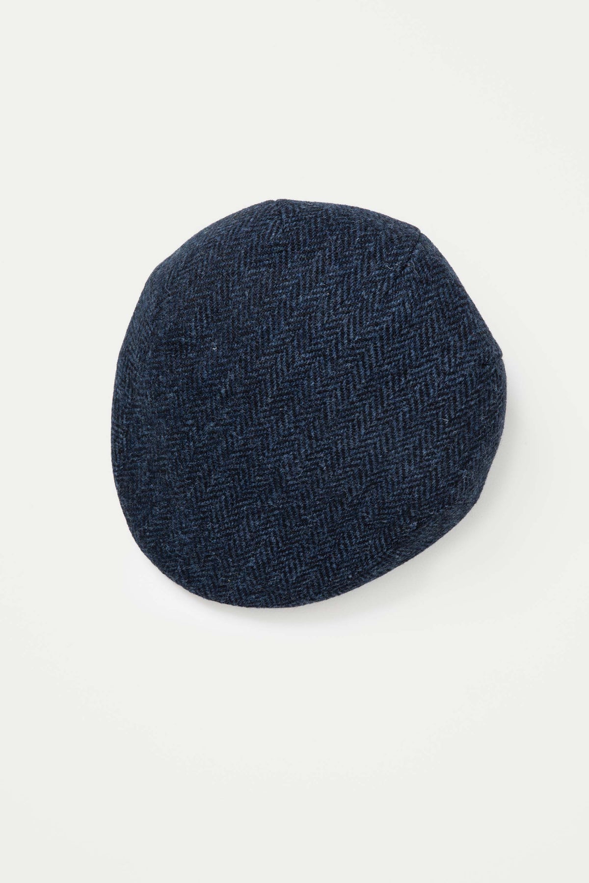 Harris Tweed Stornoway Cap in dark navy herringbone, top-down view showing the textured wool weave pattern
