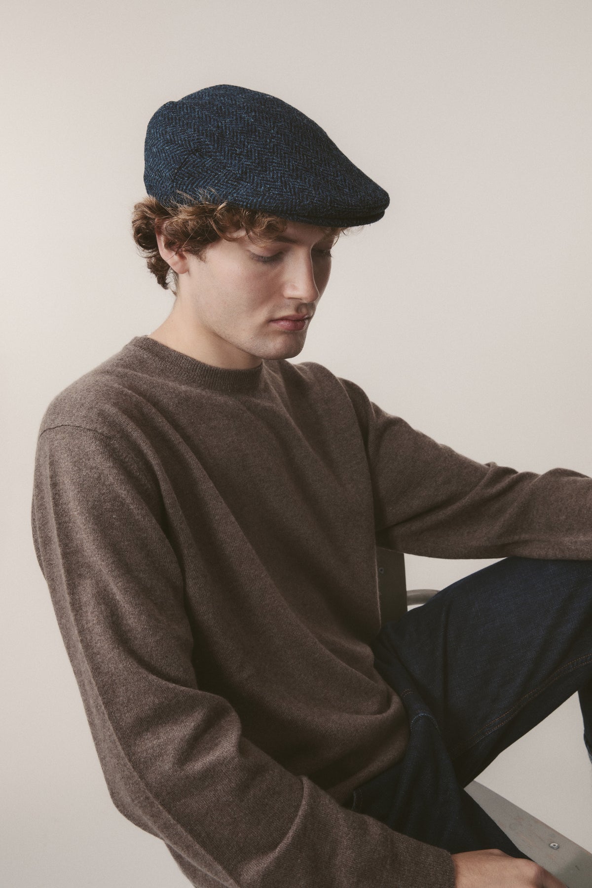 Harris Tweed Stornoway Cap in dark navy herringbone worn by a male model, showcasing the classic flat cap silhouette and stitched peak