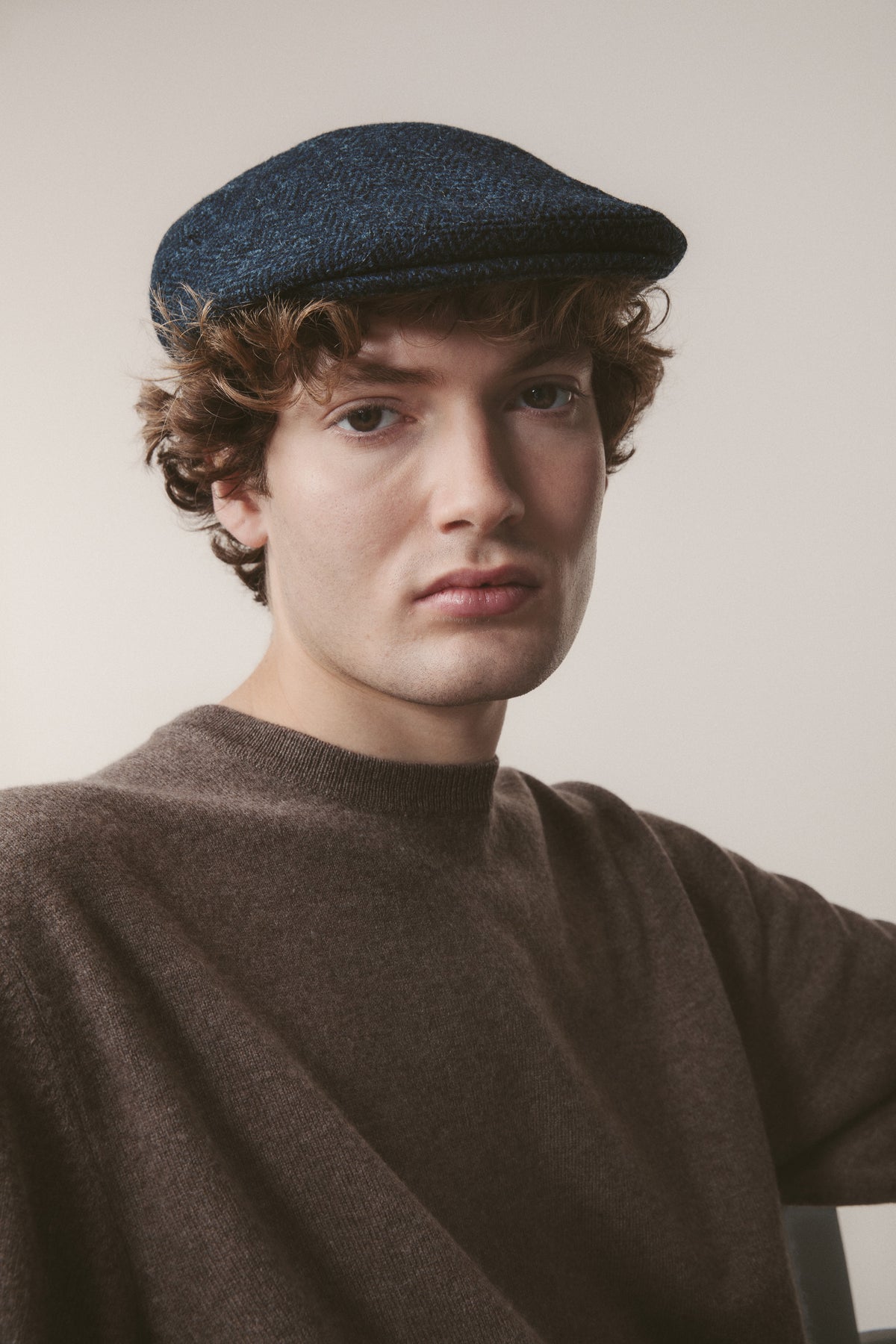 Harris Tweed Stornoway Cap in dark navy herringbone worn by model, front view showing the flat cap's low profile and textured weave