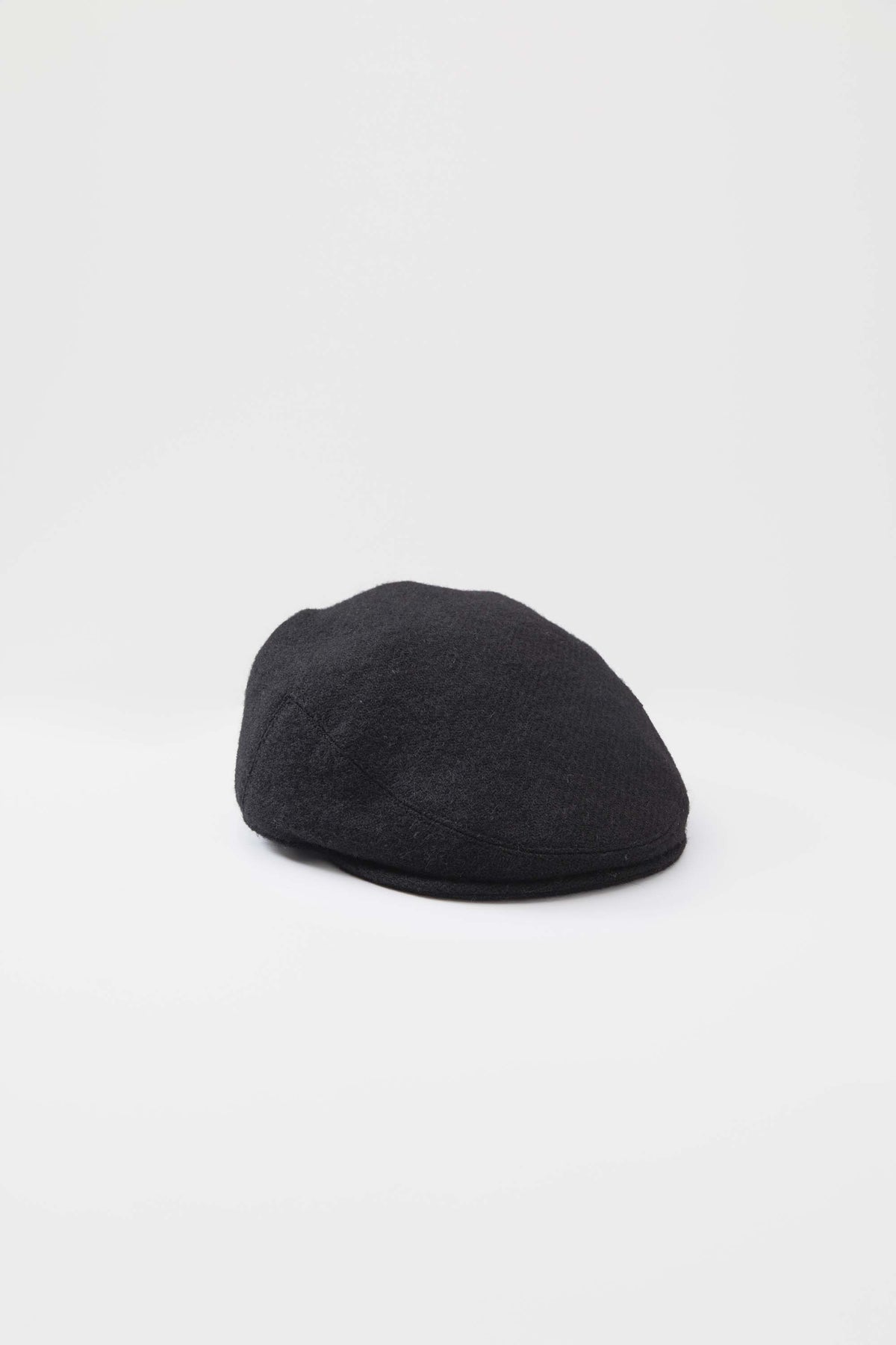 Harris Tweed Stornoway Cap in plain black twill, front three-quarter view showing low-profile flat cap silhouette and seam detail