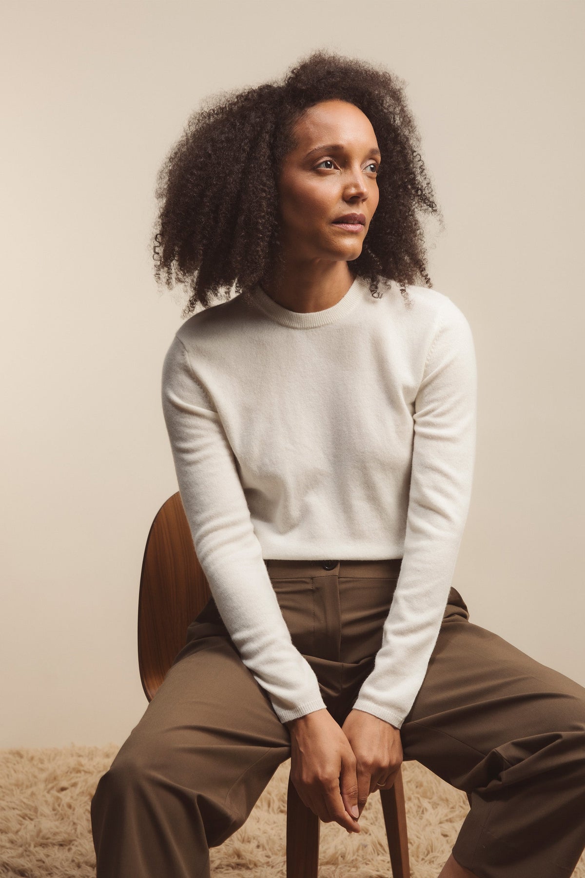 Women's Cashmere Crew Neck Jumper in Soft Cream styled on a seated model, showing the relaxed fit and ribbed cuffs