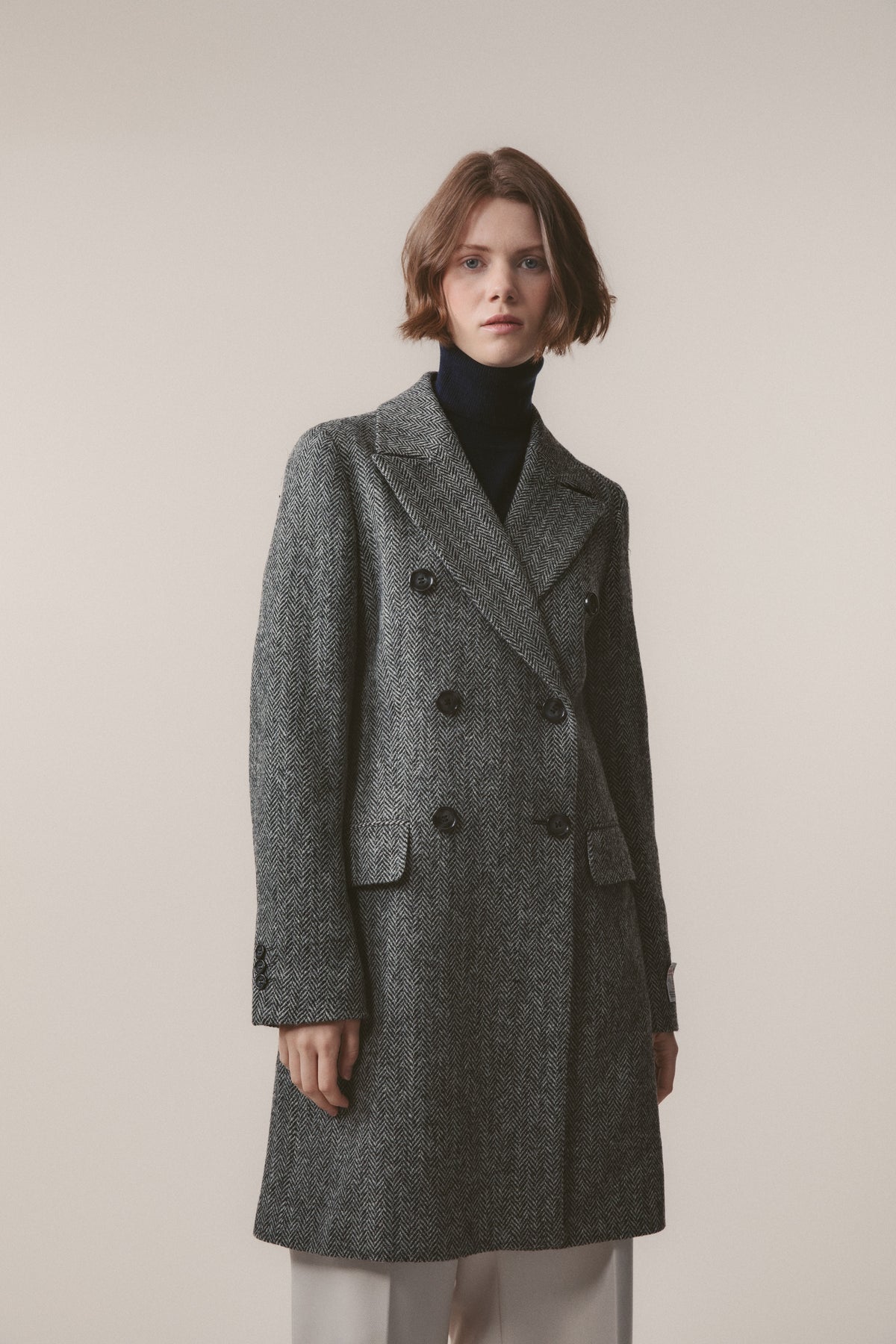 Women's Harris Tweed Melody Coat in light grey herringbone, double-breasted with peaked lapels and dark buttons, knee length