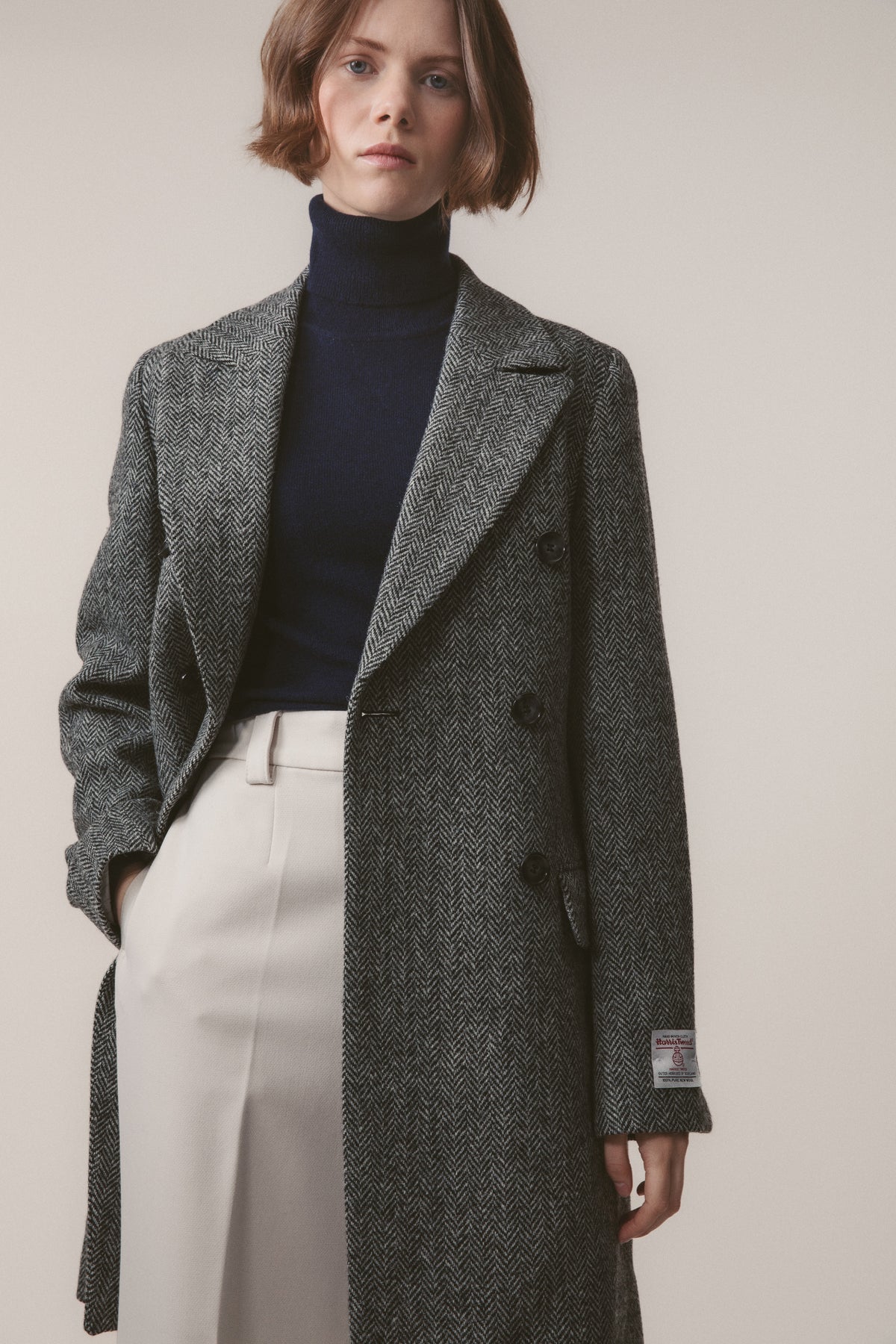 Women's Harris Tweed Melody Coat in Light Grey Herringbone worn open, showing double-breasted button front and Harris Tweed label