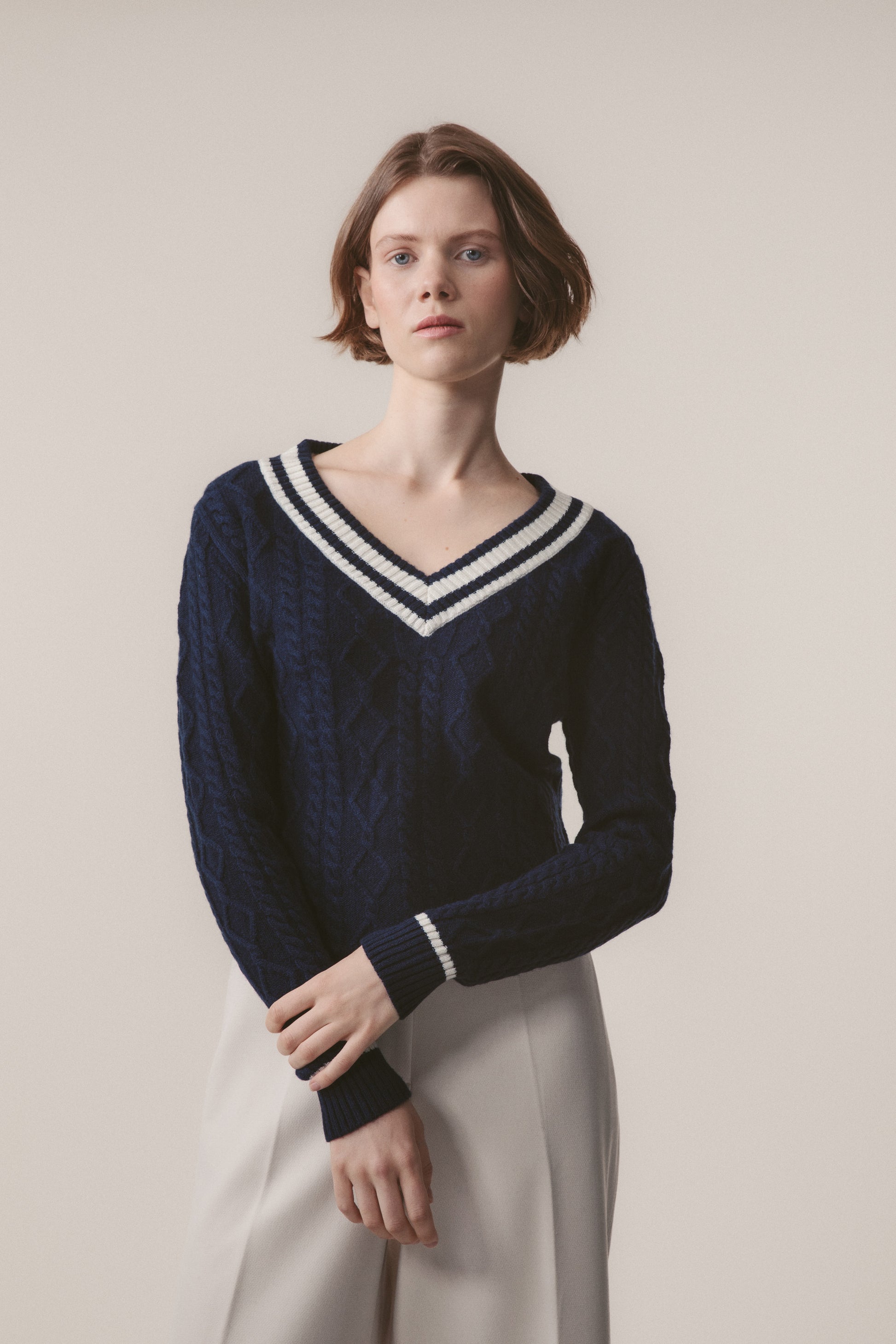 Model wearing Women's Cashmere Cricket Style Jumper in navy with cream striped V-neck and cuffs, showing cable-knit texture detail
