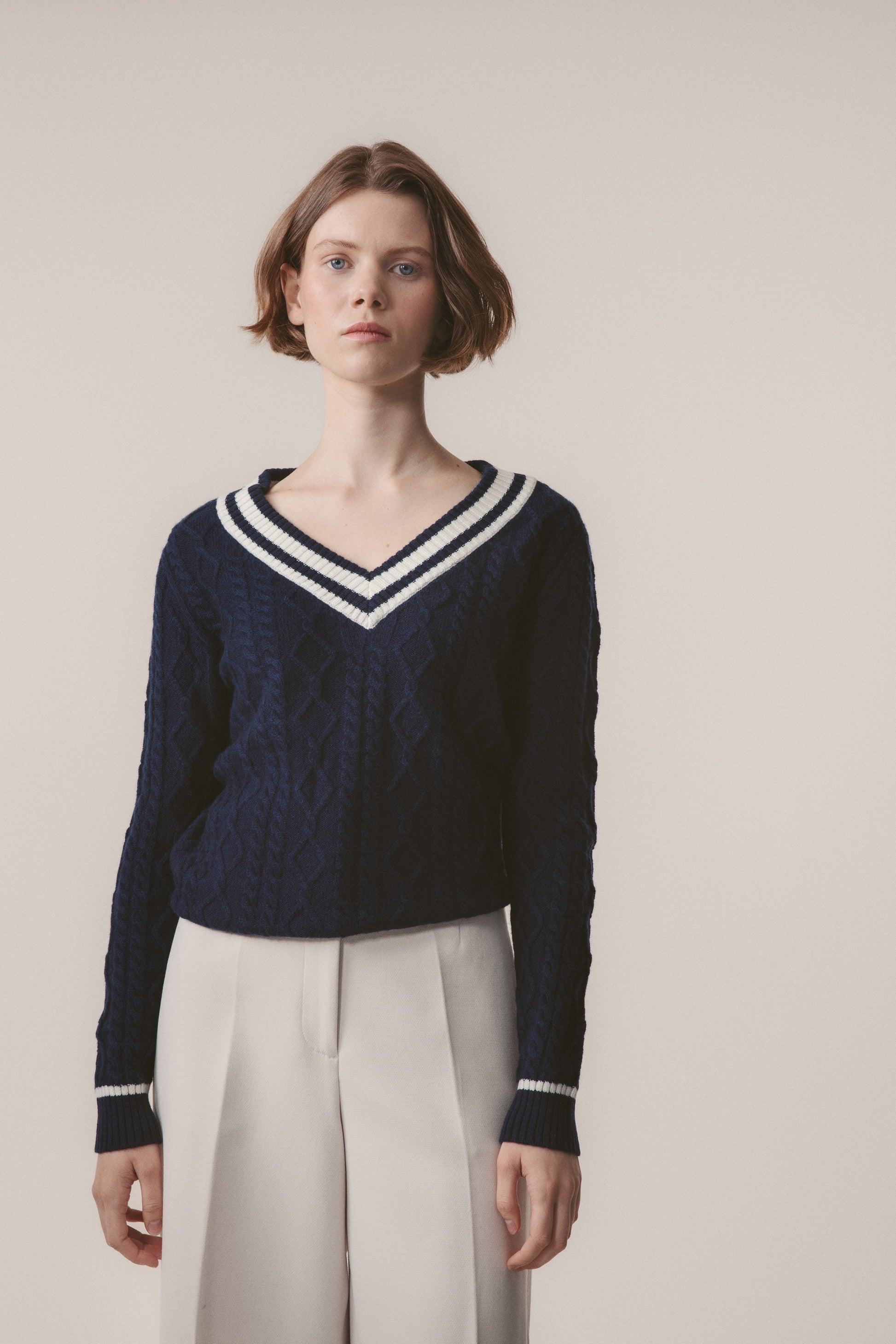 Model wearing Women's Cashmere Cricket Style Jumper in navy with cream striped V-neck and cuffs, paired with white trousers