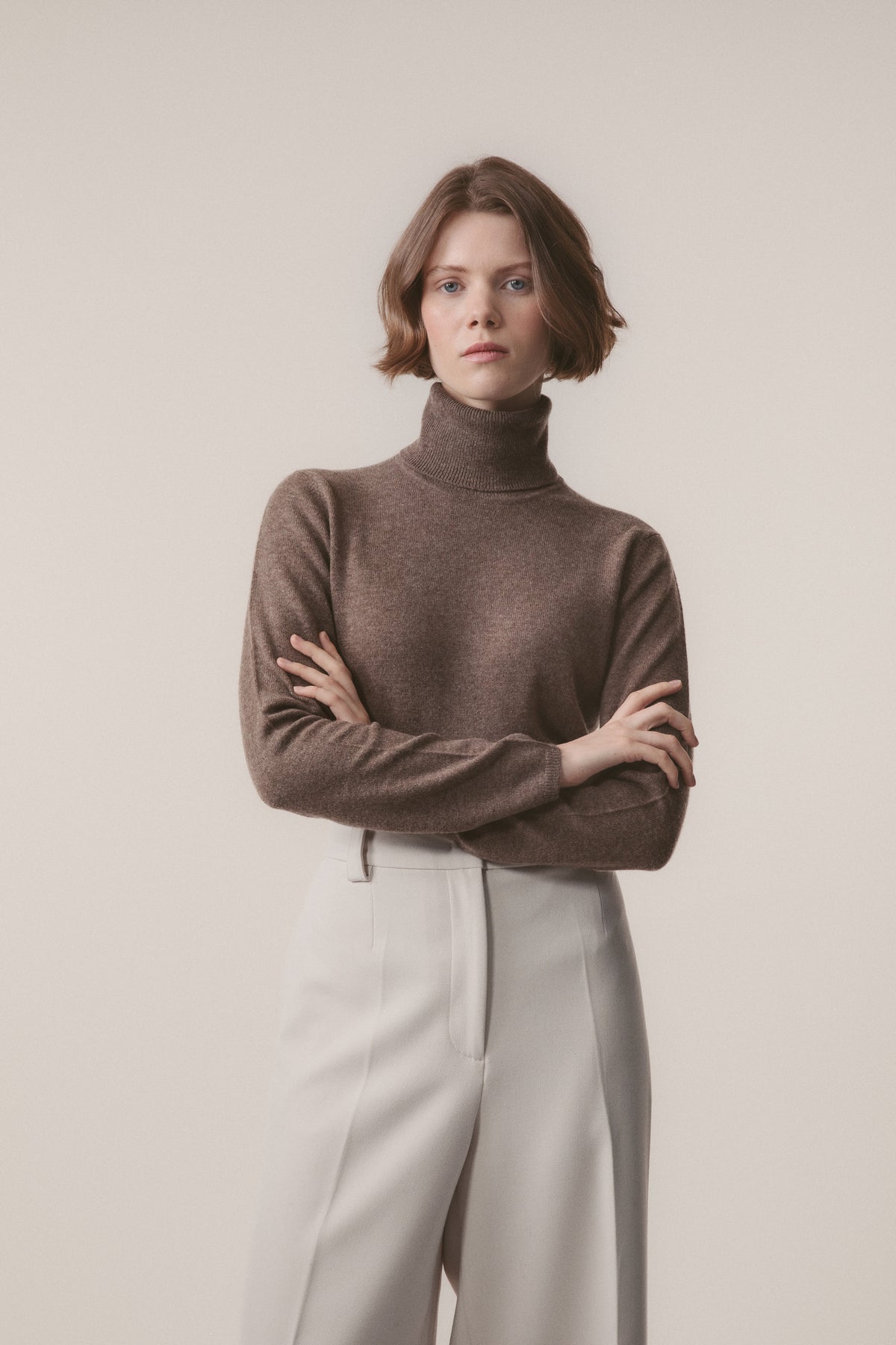 Women's Cashmere Polo Neck Jumper in Squirrel brown, front view with arms crossed showing relaxed fit and ribbed collar