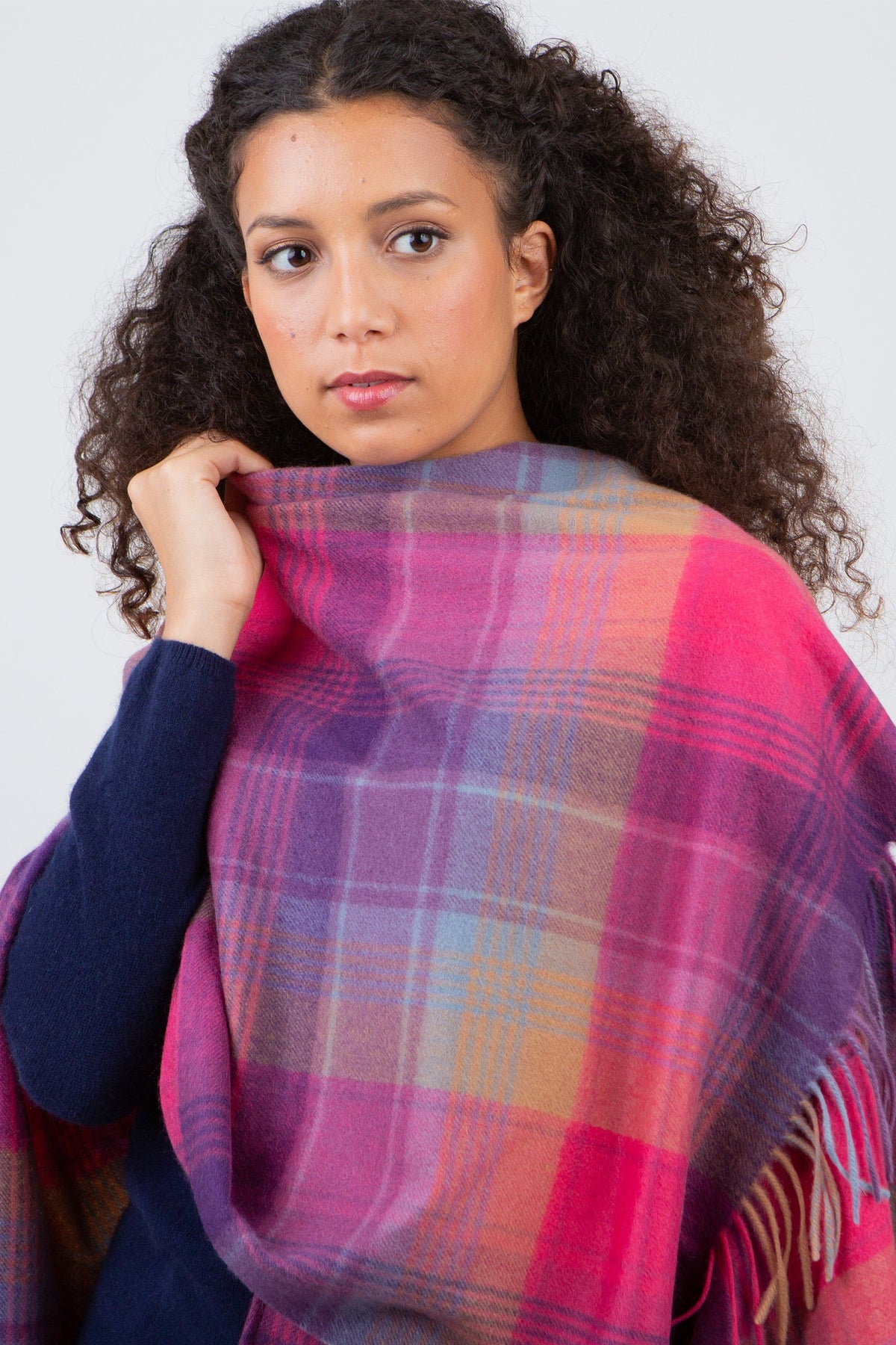 Model wearing Repeat Edge Cashmere Wrap in Pink, showing the vibrant pink, purple, and blue tartan pattern with fringed edge