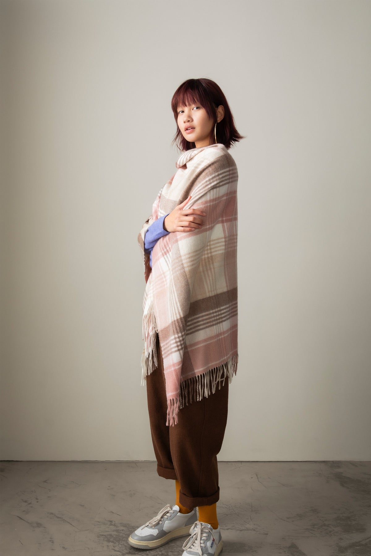 Model wearing Repeat Edge Cashmere Wrap in Natural draped over shoulders, showing pink and beige tartan pattern with fringed hem