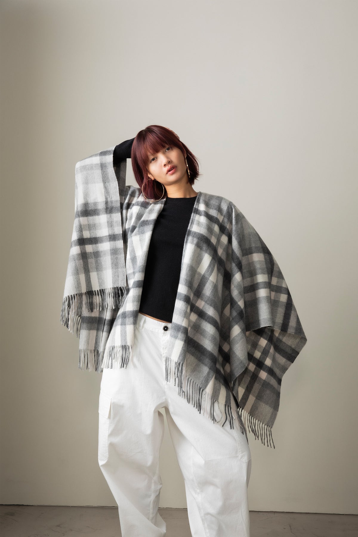 Stepping Check Cashmere Wrap in Monochrome worn open as a poncho, showing grey and white plaid pattern with fringed edges