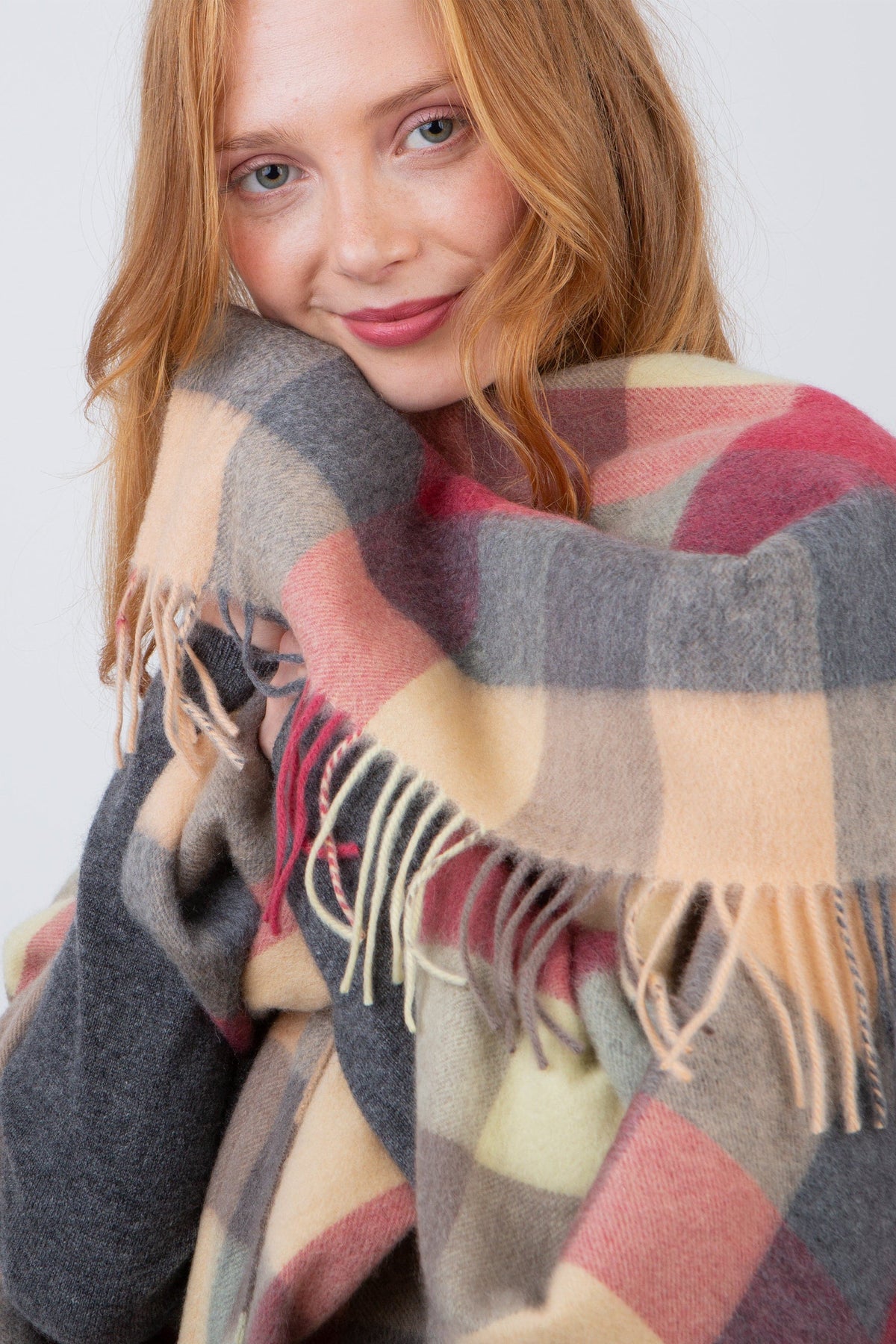 Model snuggling the 5 Square Cashmere Wrap - Grey Rose, showing soft fringed edges and plaid pattern in grey, pink, and cream