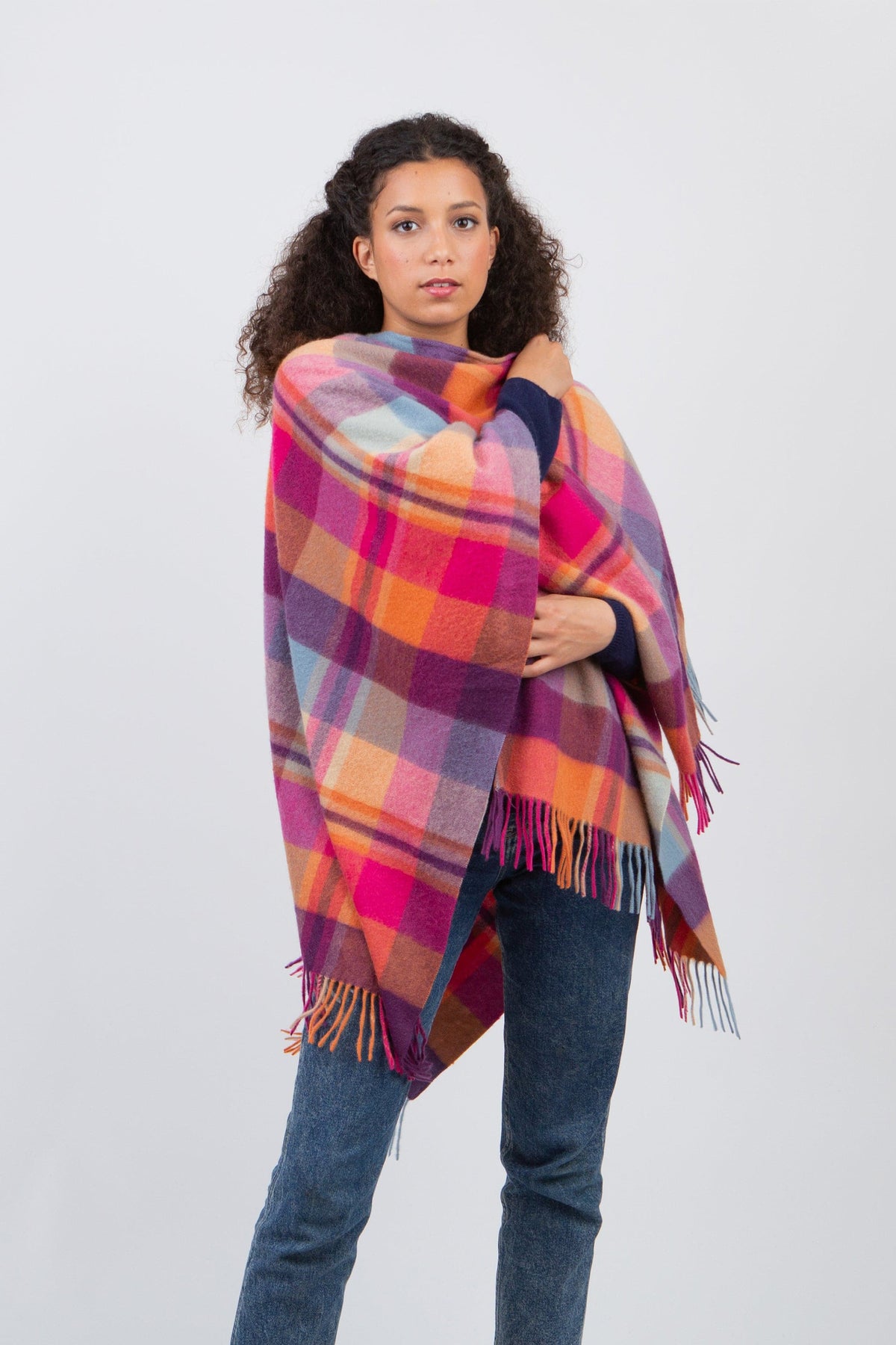 Square Check Lambswool Wrap in Orient Ginger, a vibrant pink, orange, purple, and blue plaid wrap with fringed edges, modelled draped over shoulders