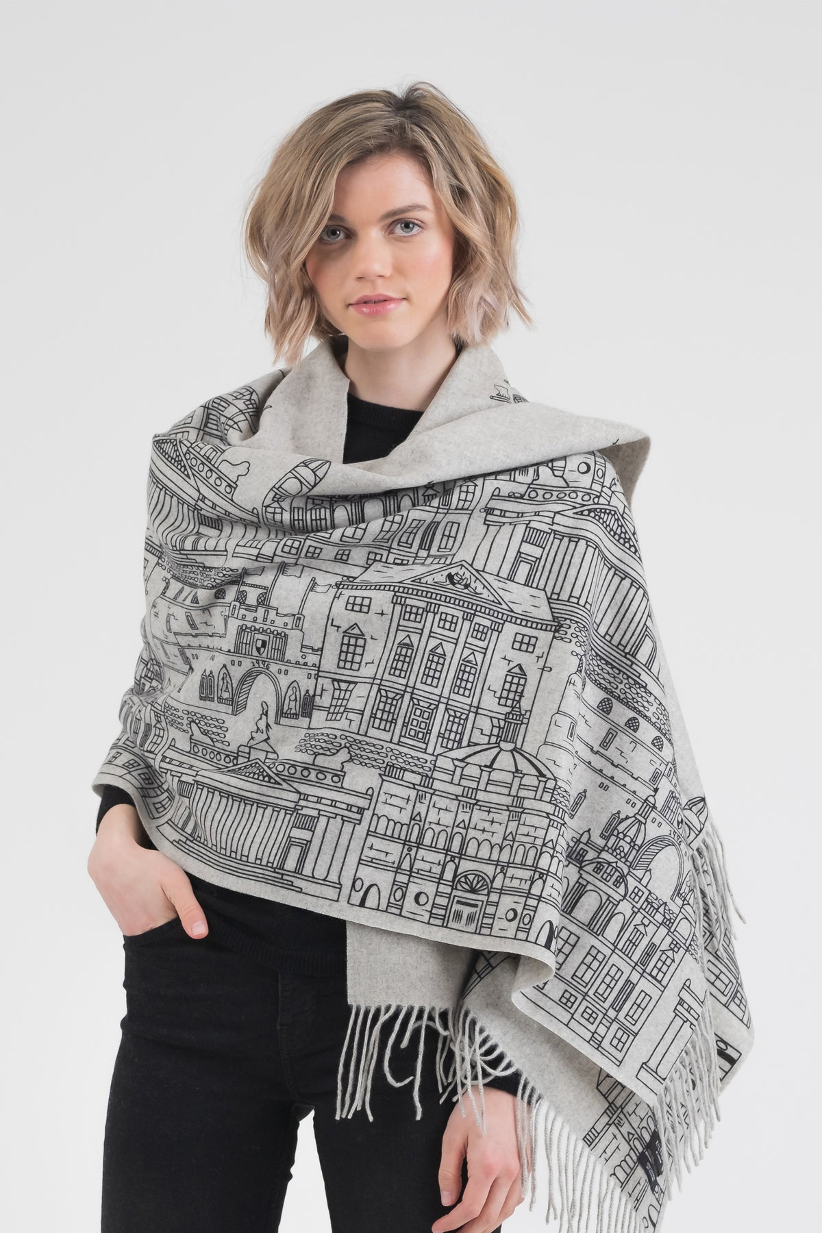 Skyline Cashmere Double Sided Stole in grey, worn as a wrap showing black hand-printed Edinburgh skyline illustrations and fringed edges