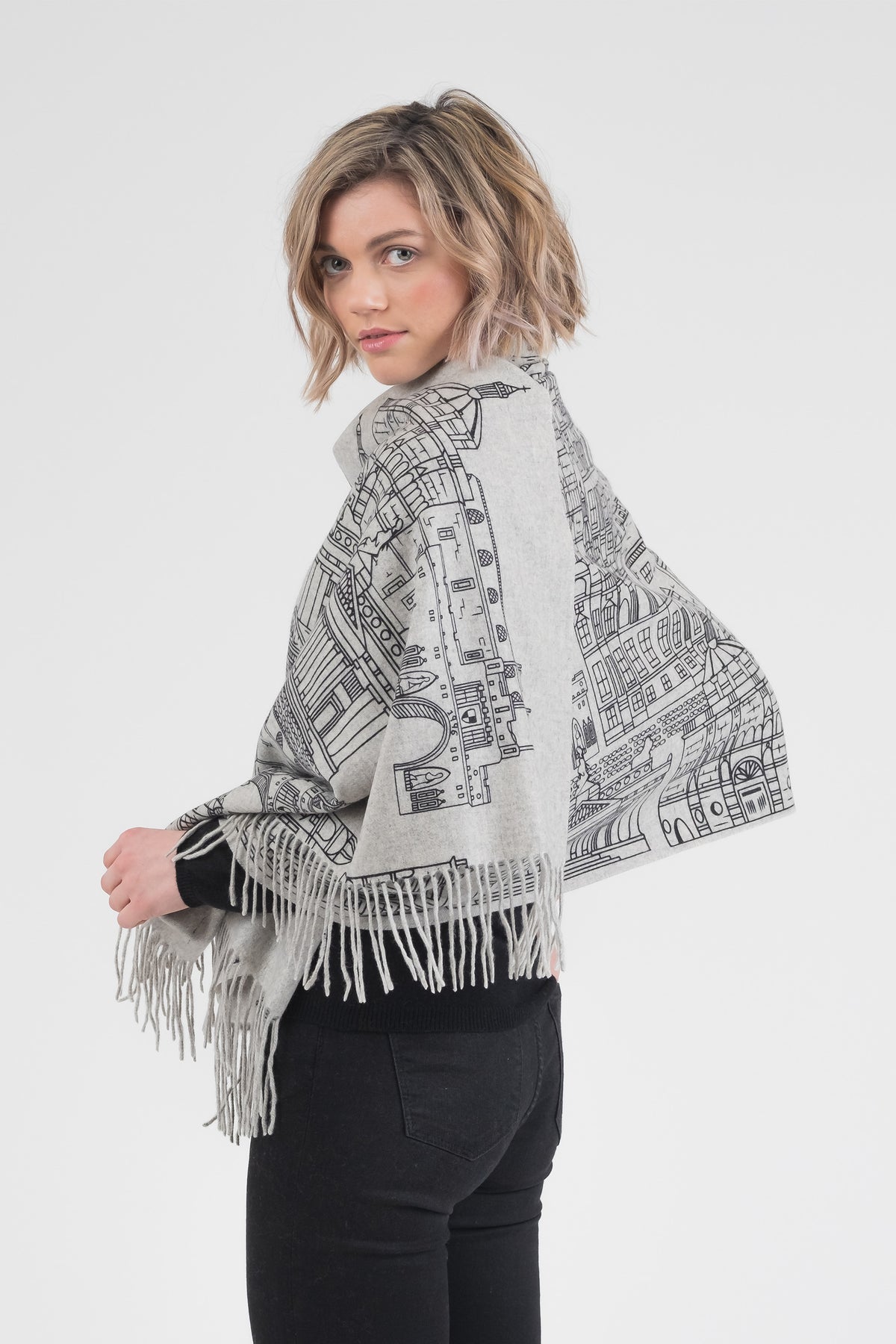 Skyline Cashmere Double Sided Stole in Grey Repeat worn as a wrap, showing back view with detailed cityscape illustration and fringe hem