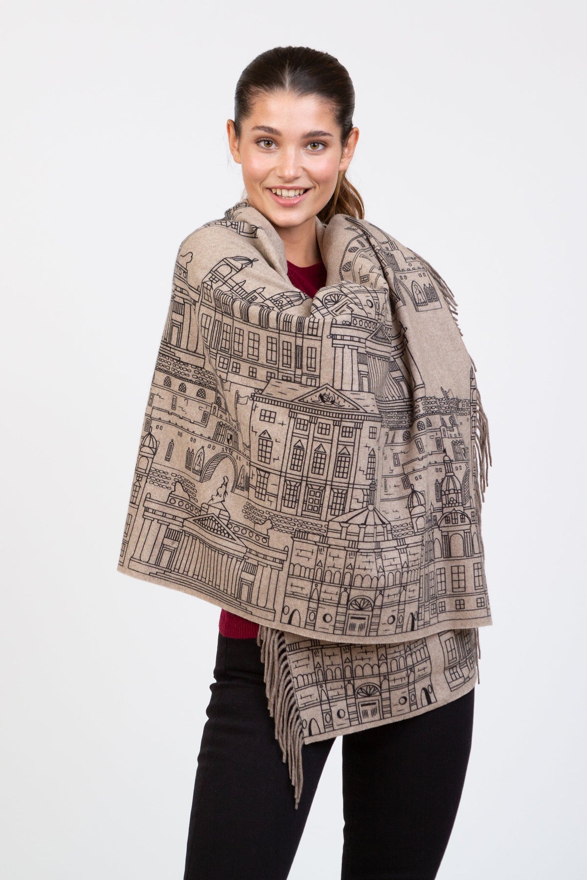 Skyline Cashmere Double Sided Stole in Beige Repeat, featuring handprinted architectural illustrations, with fringed edges, worn wrapped around shoulders