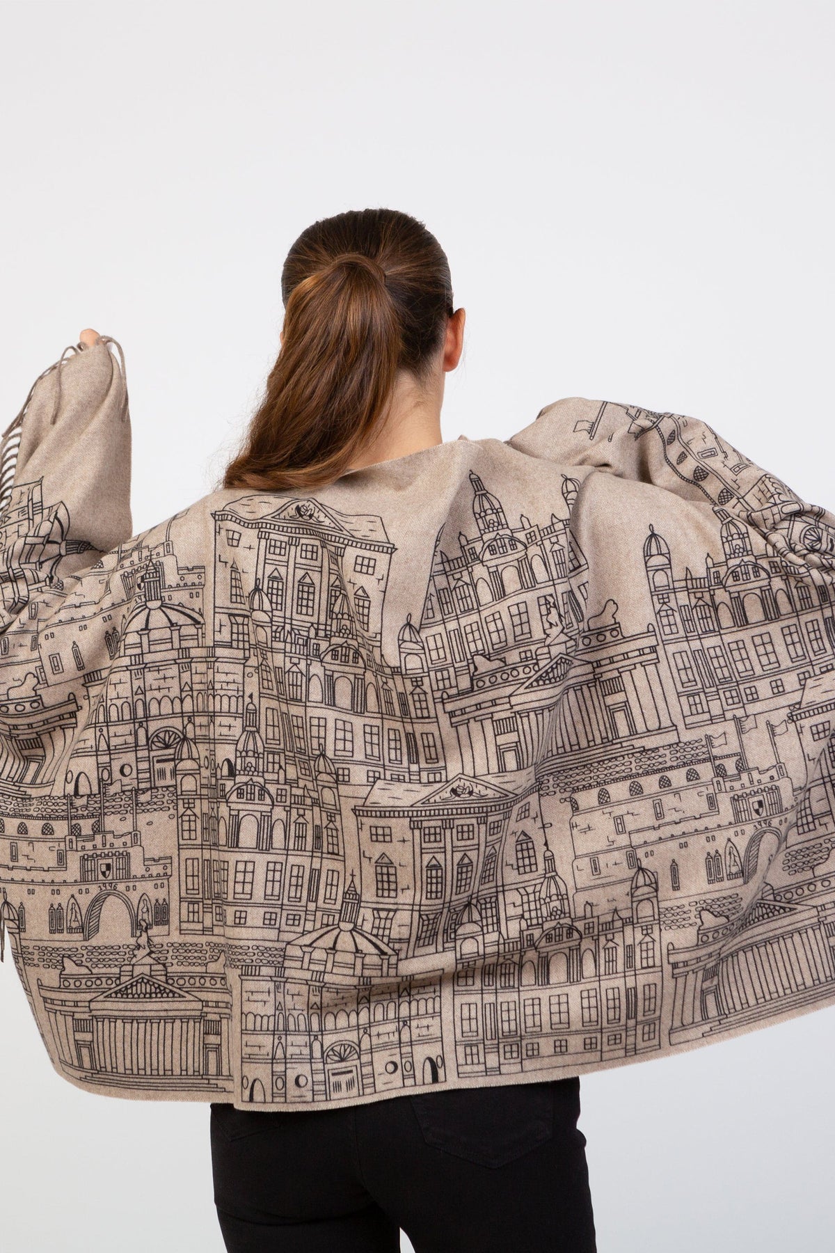 Back view of model draping Skyline Cashmere Double Sided Stole in Beige Repeat, showcasing detailed cityscape illustration