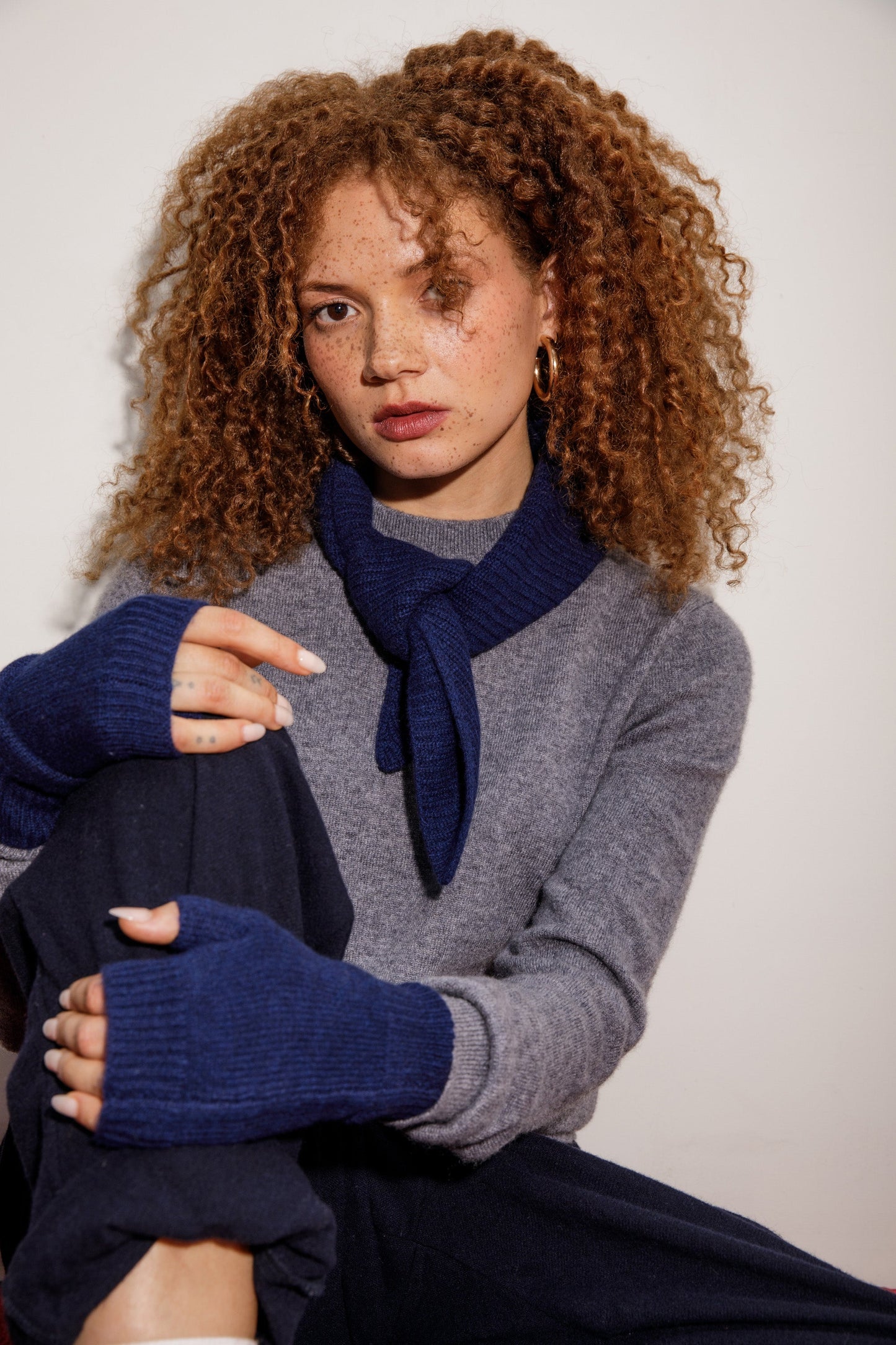Knitted Cashmere Neck Tie in Cosmos styled knotted at the neck, paired with grey sweater and matching navy fingerless gloves