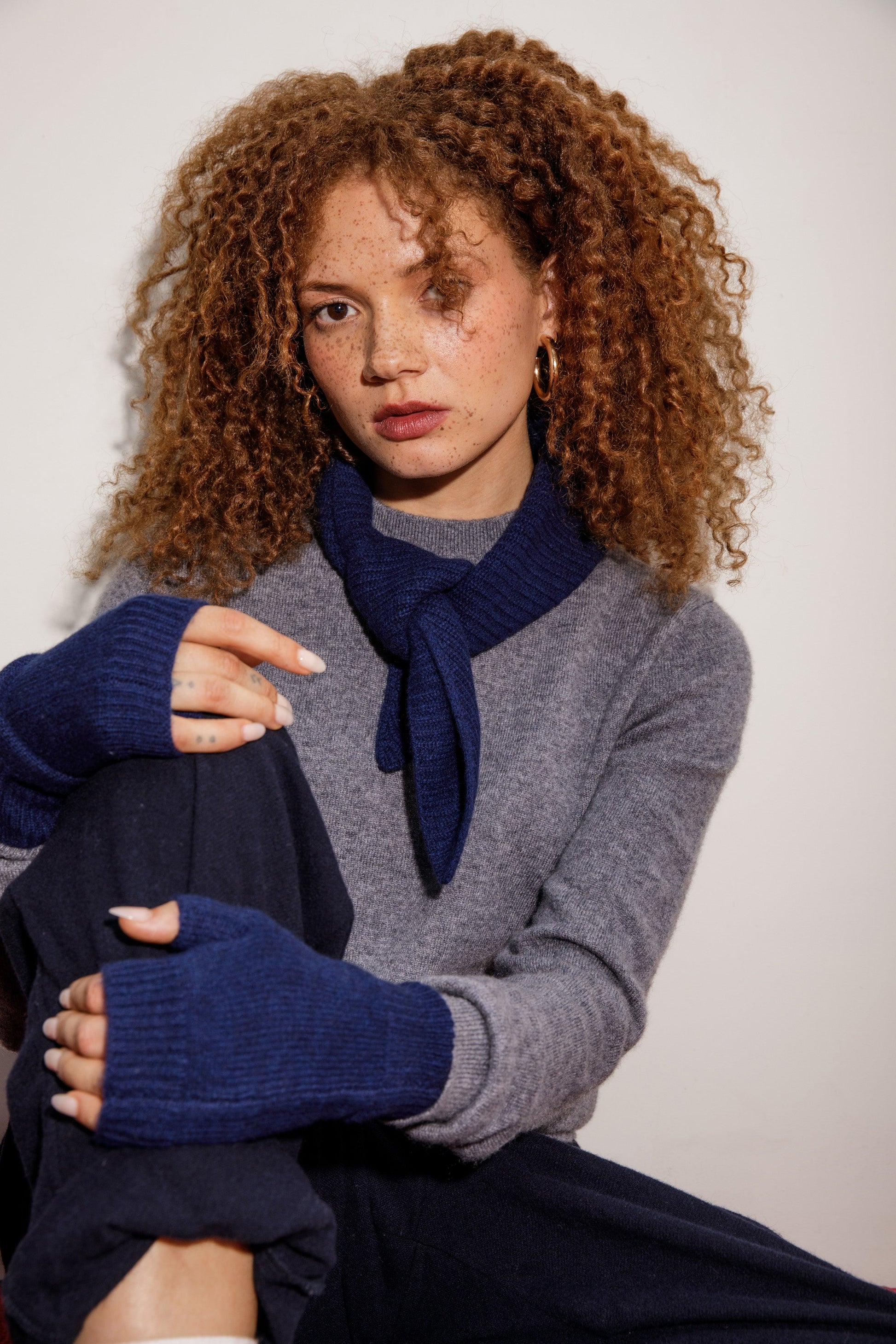Knitted Cashmere Neck Tie in Cosmos styled knotted at the neck, paired with grey sweater and matching navy fingerless gloves