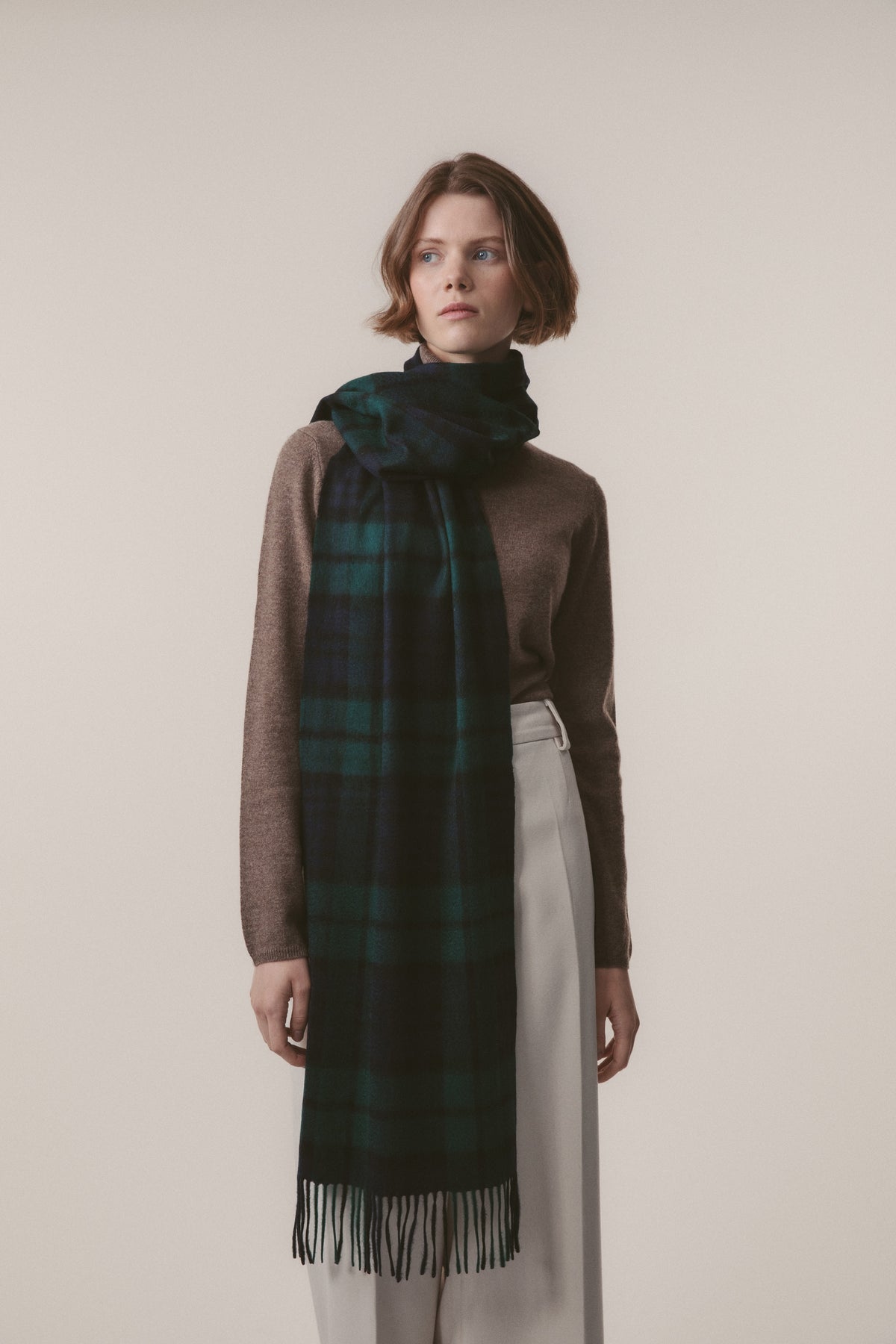 Heritage Tartan Cashmere Wide Scarf in Blackwatch worn draped around the neck, showing deep green and navy plaid with fringed ends