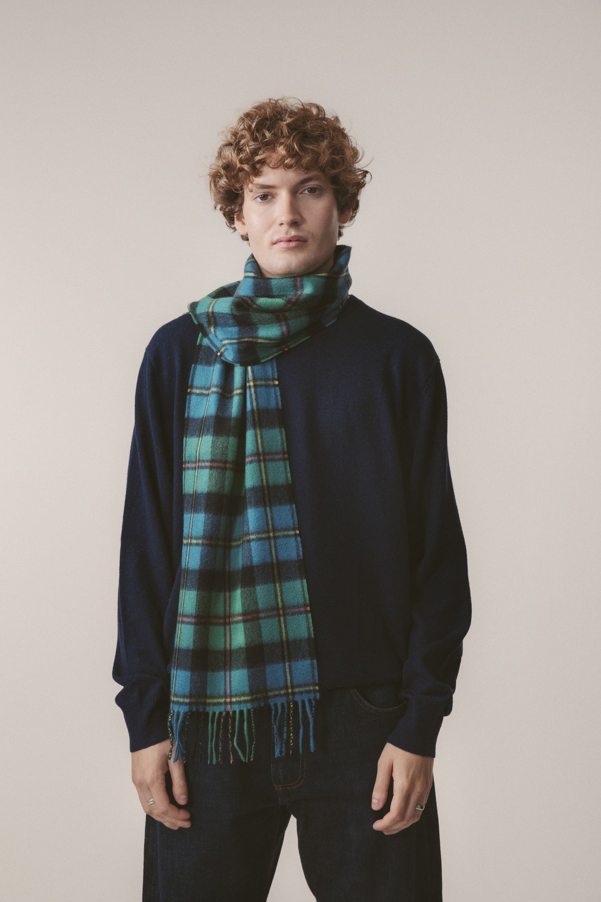Heritage Tartan Cashmere Scarf in Macleod Antique, green and blue tartan with fringed ends, worn draped over a navy sweater