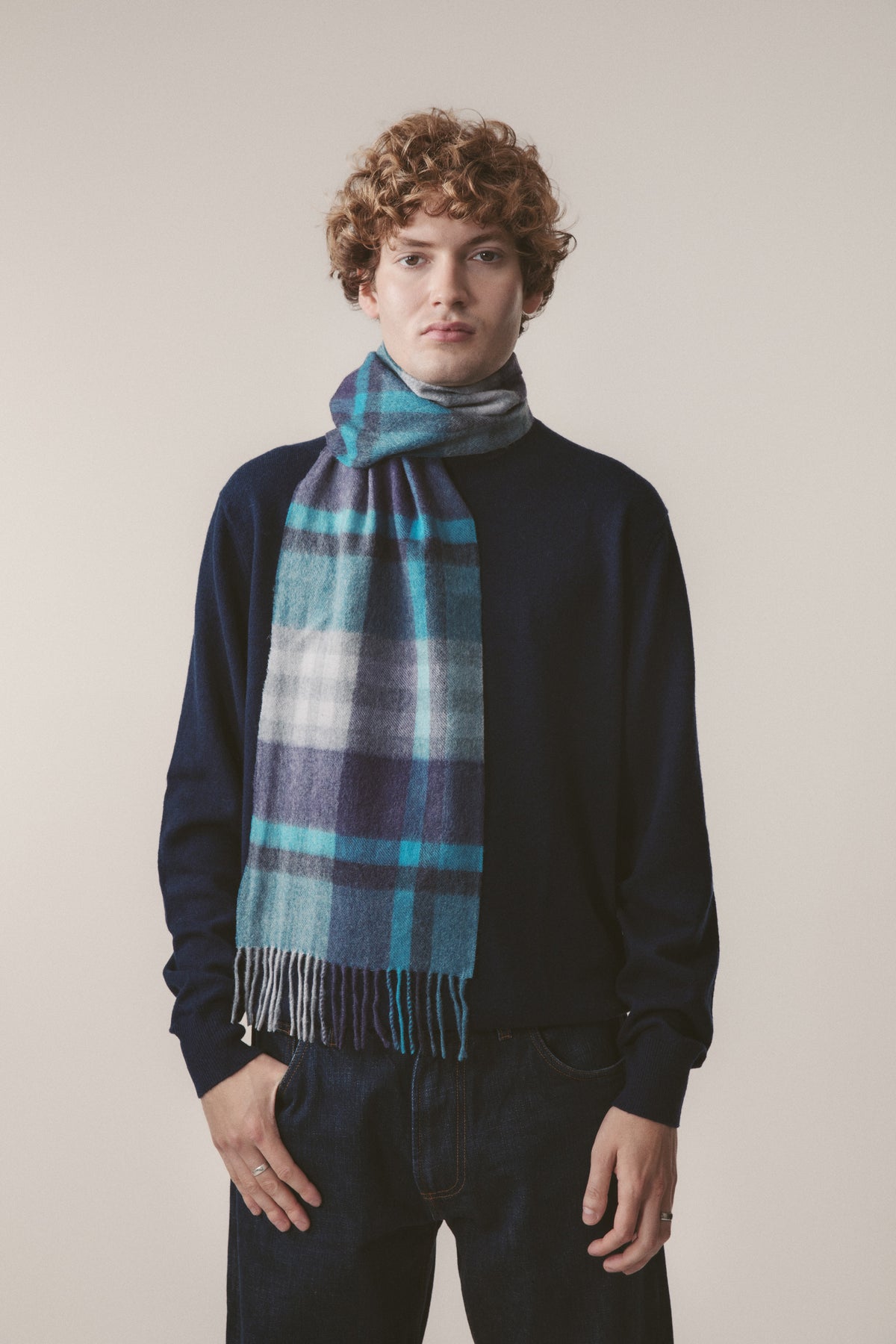 Tartan 2 Cashmere Scarf in Blue worn by model, featuring navy, turquoise, and white plaid pattern with fringed ends