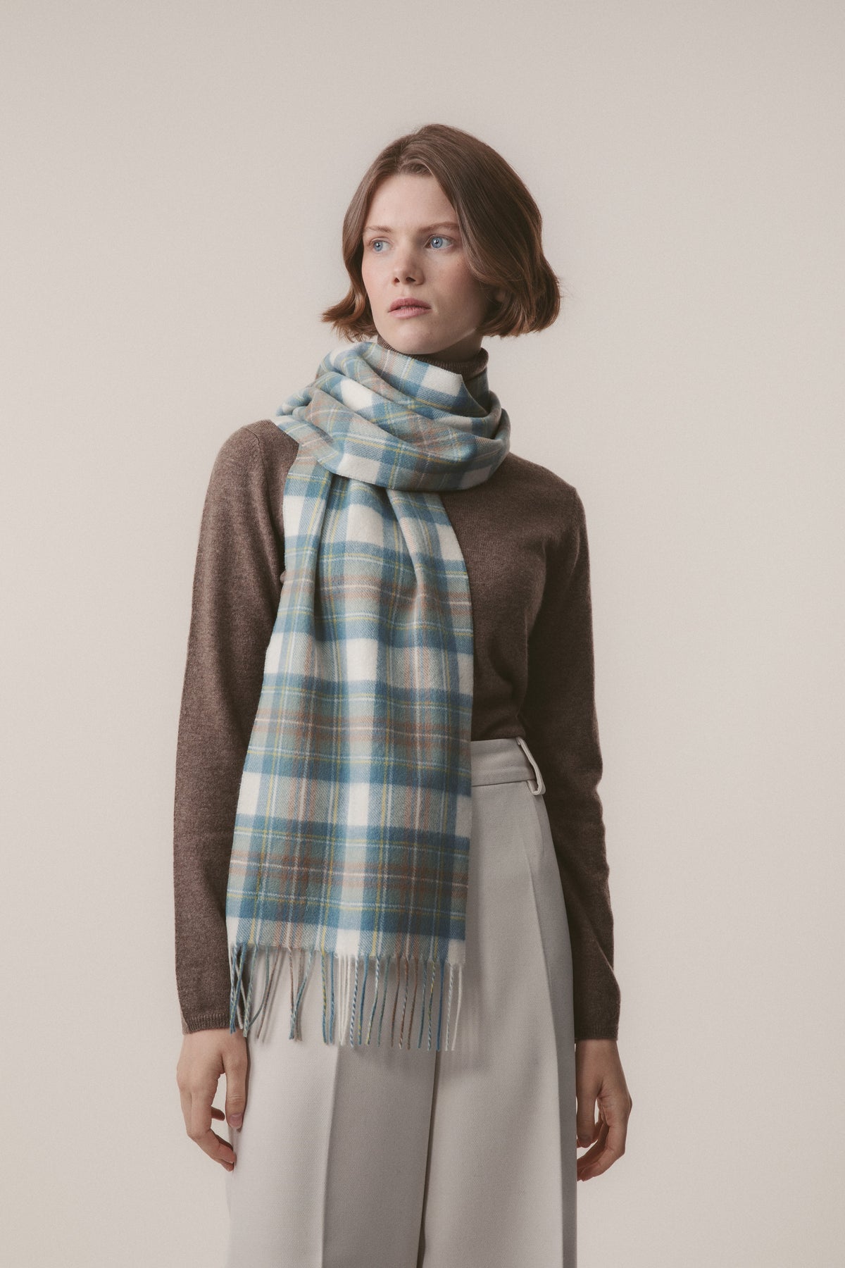 Heritage Tartan Cashmere Scarf in Muted Stewart worn looped around the neck, showing blue and cream plaid pattern with fringed ends