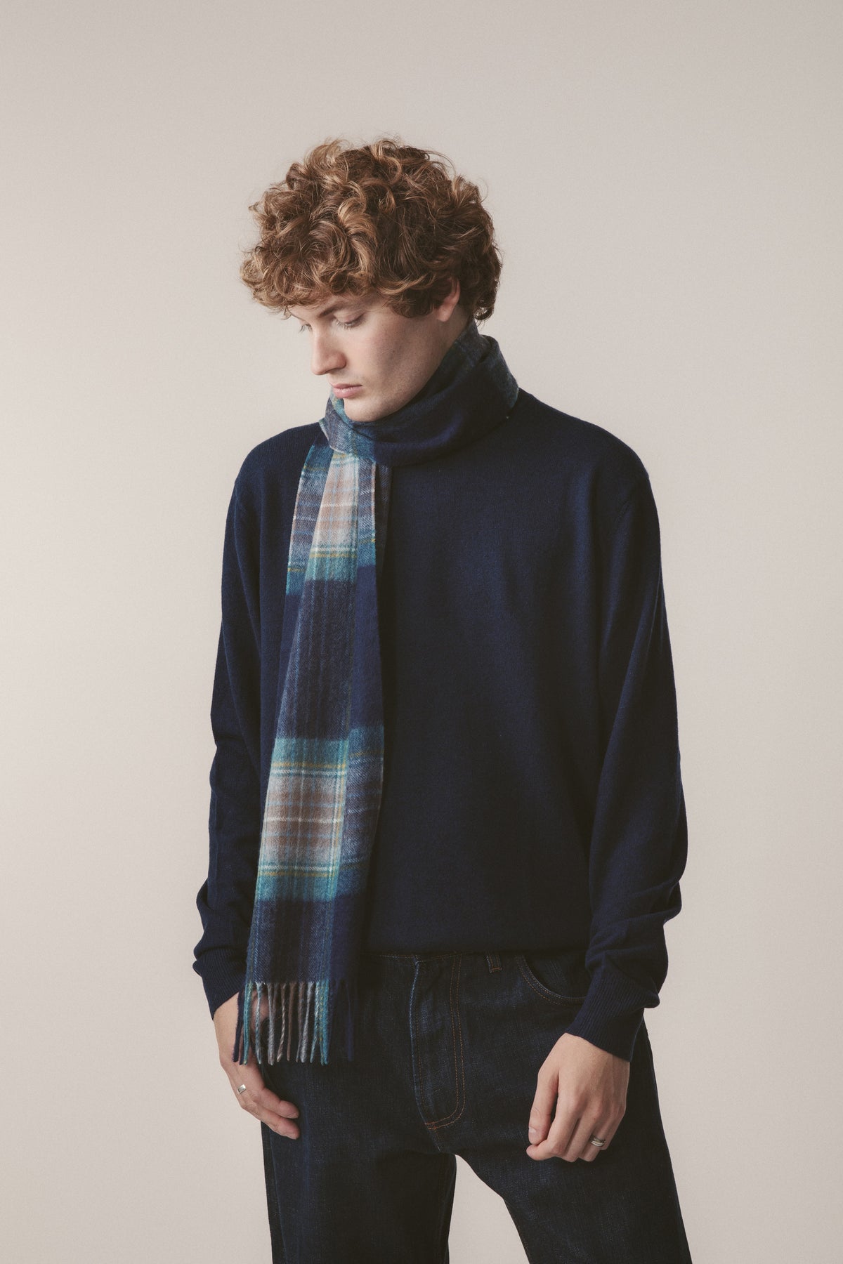 Heritage Tartan Cashmere Scarf - Holyrood worn loosely over a navy turtleneck, showing blue tartan pattern and fringed ends